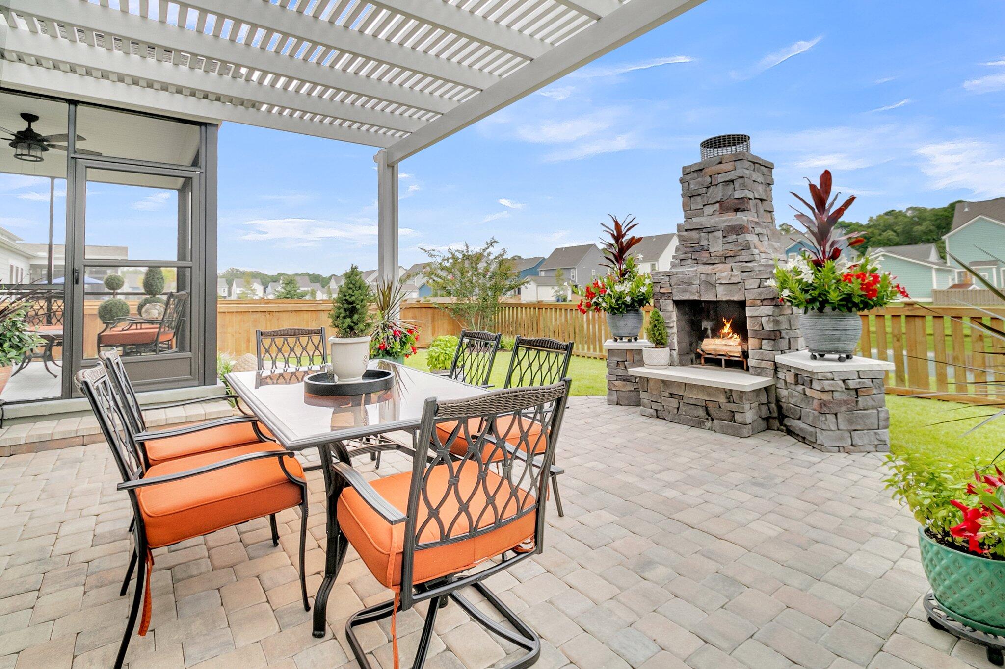 Pergola-covered patio with orange-cushioned dining chairs and a stone outdoor fireplace.