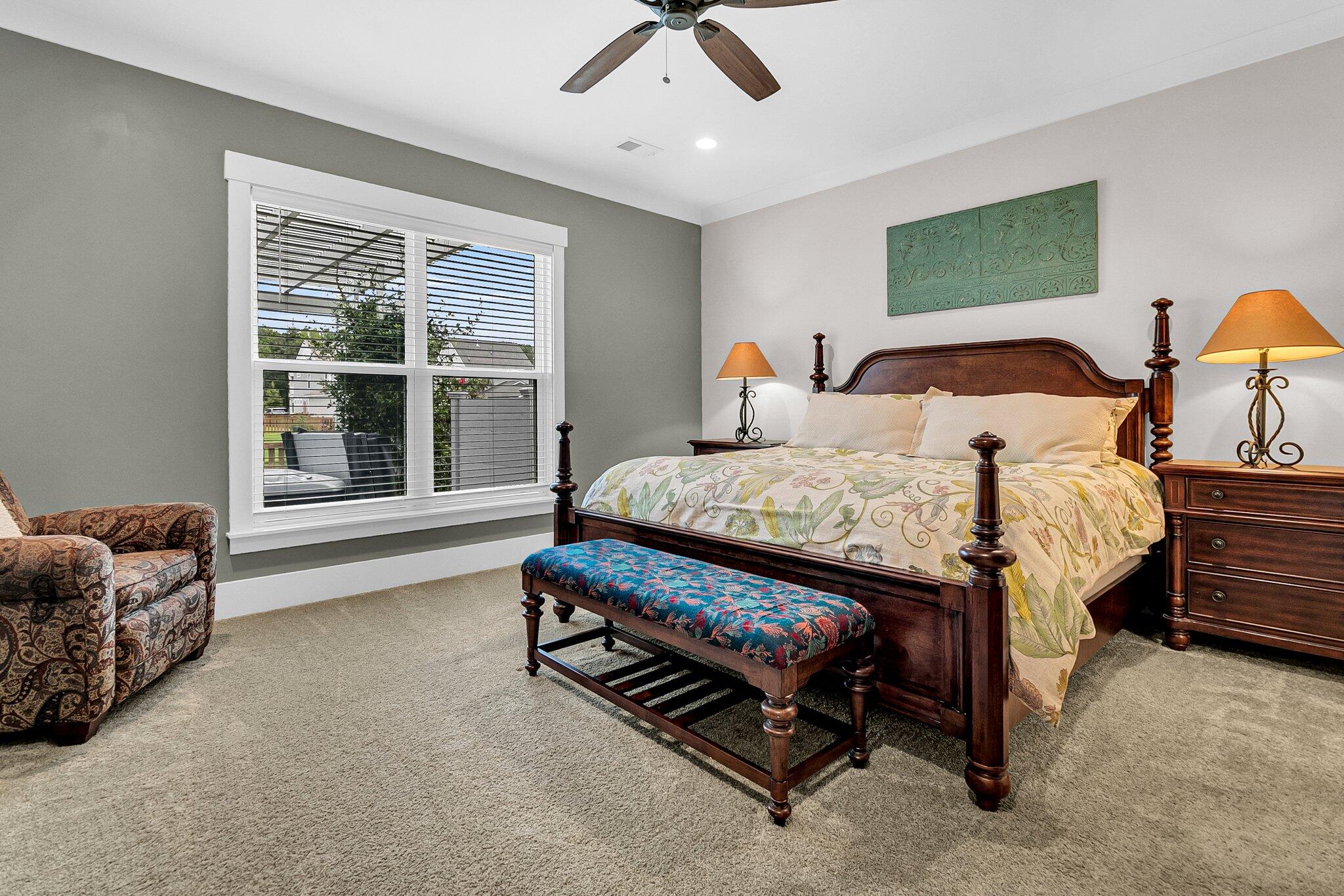 Furnished bedroom with a dark wood four-poster bed, patterned bedding, and a large window with blinds.