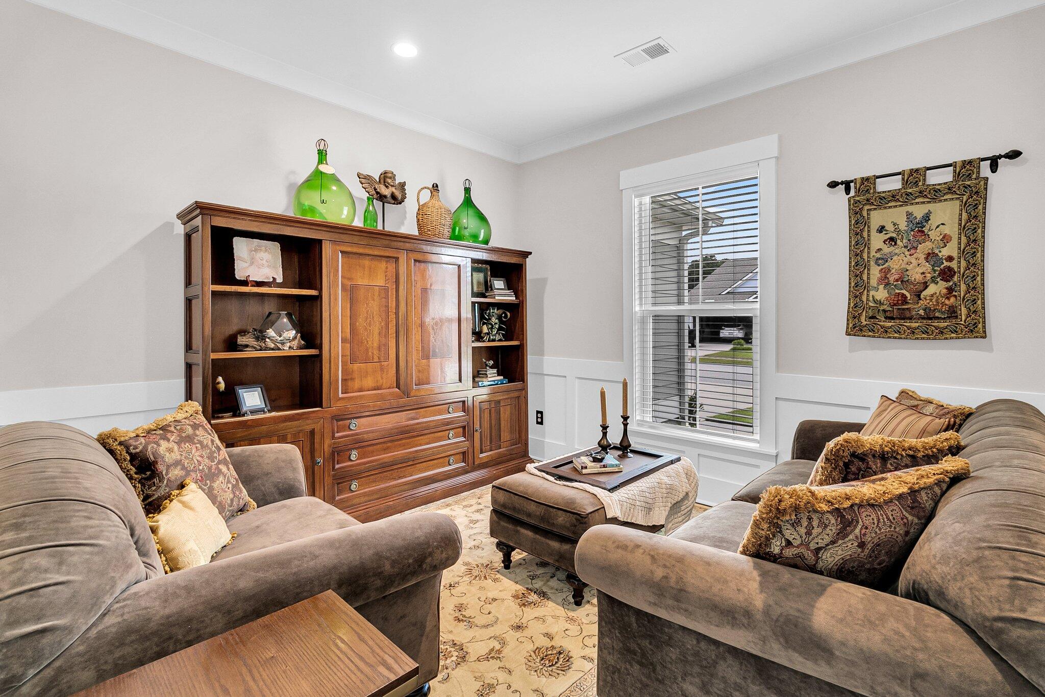 Furnished living room with taupe sofas, a wooden display cabinet, and a window with blinds.
