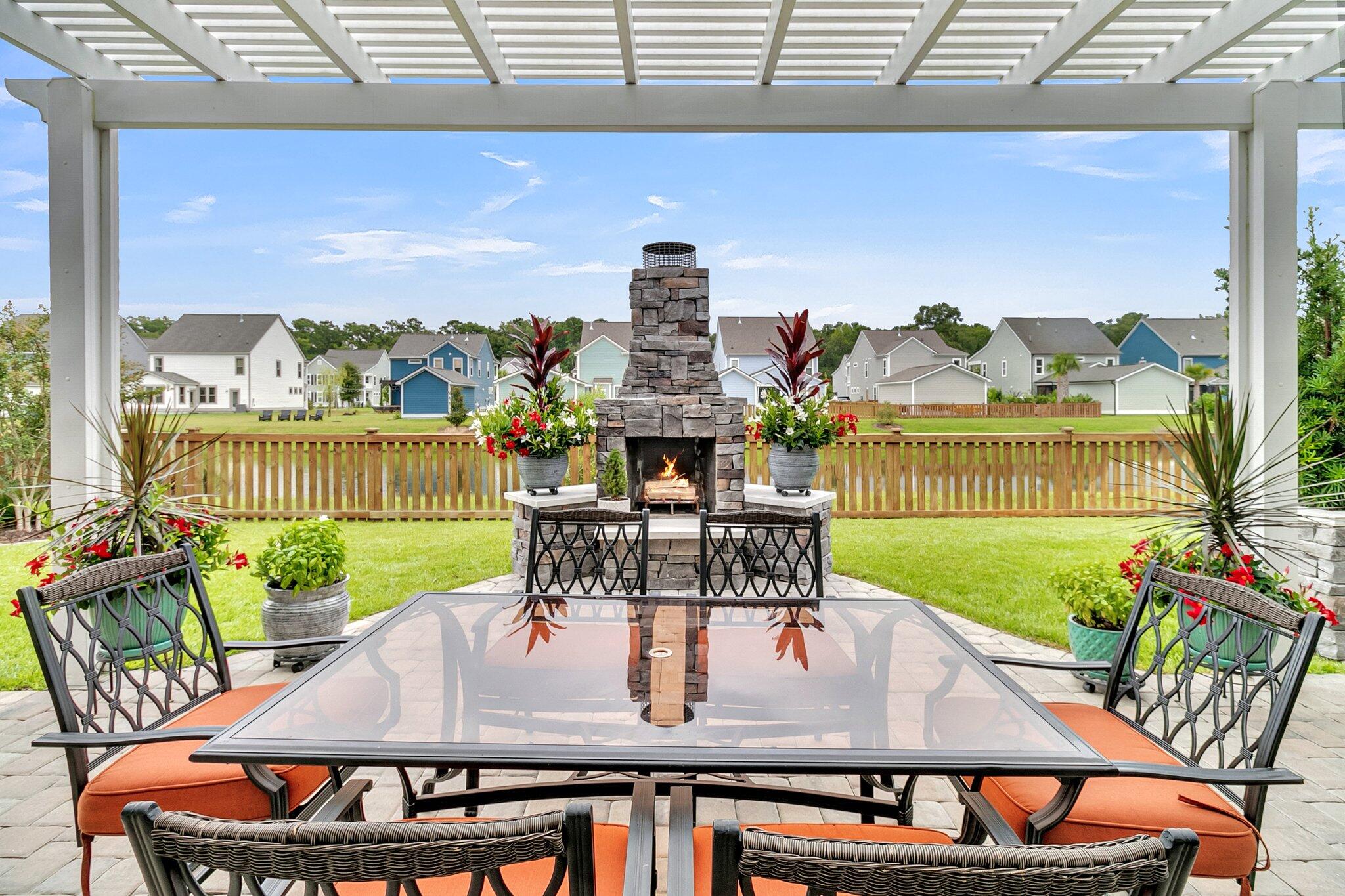 Pergola-covered patio with outdoor dining set and stone fireplace overlooking a fenced lawn.