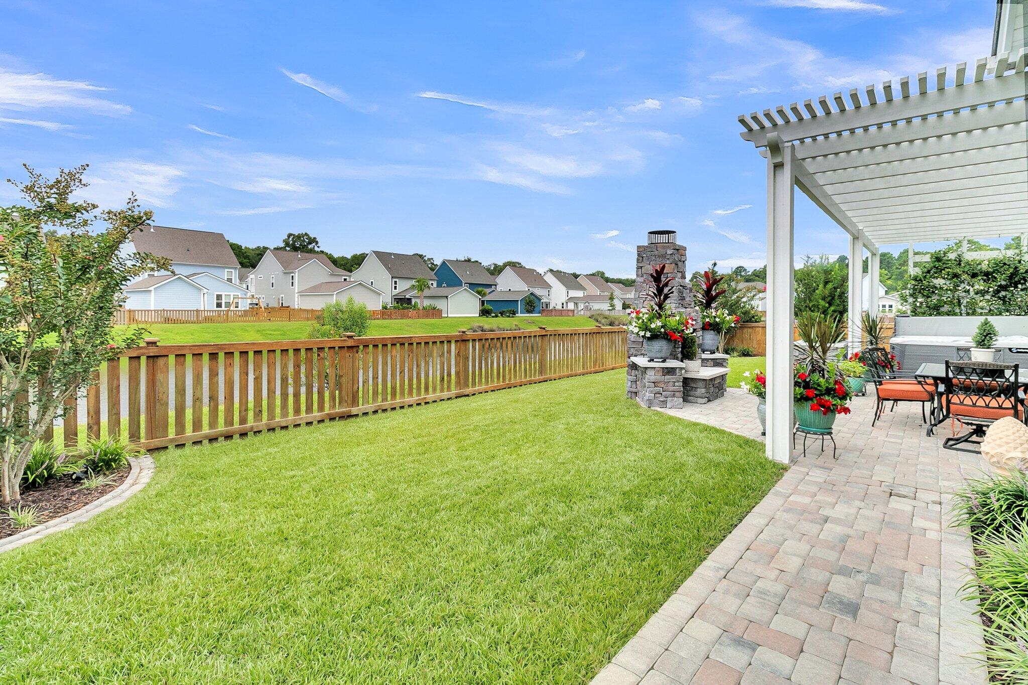 Backyard lawn and fenced patio with a white pergola, outdoor seating, and stone fireplace.