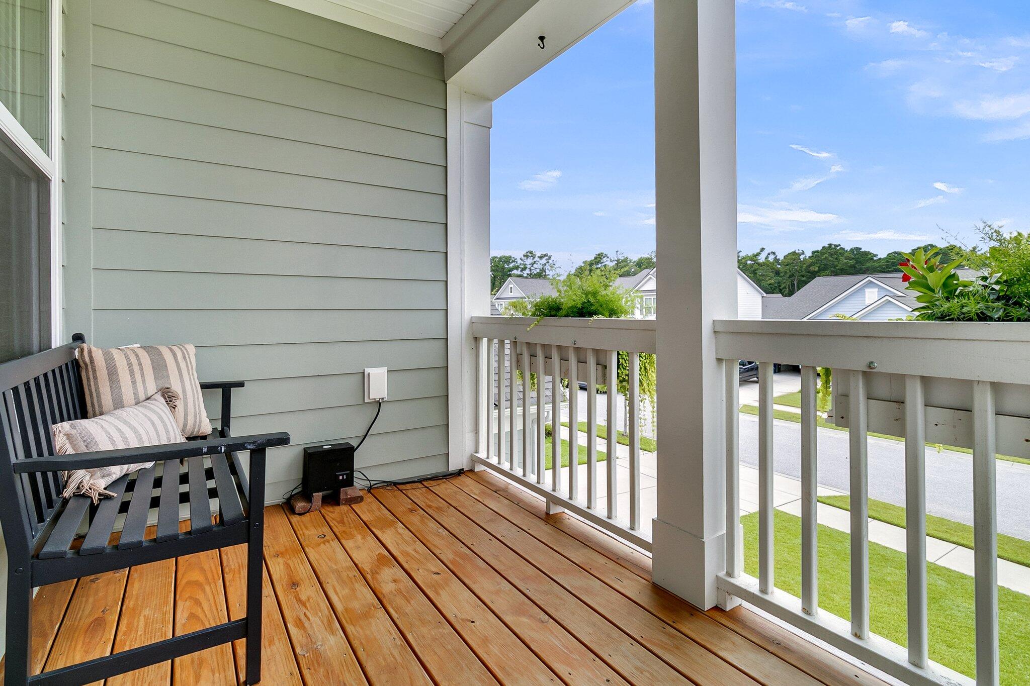 Covered porch with wood flooring, white railings, and a cushioned bench overlooking neighboring homes.