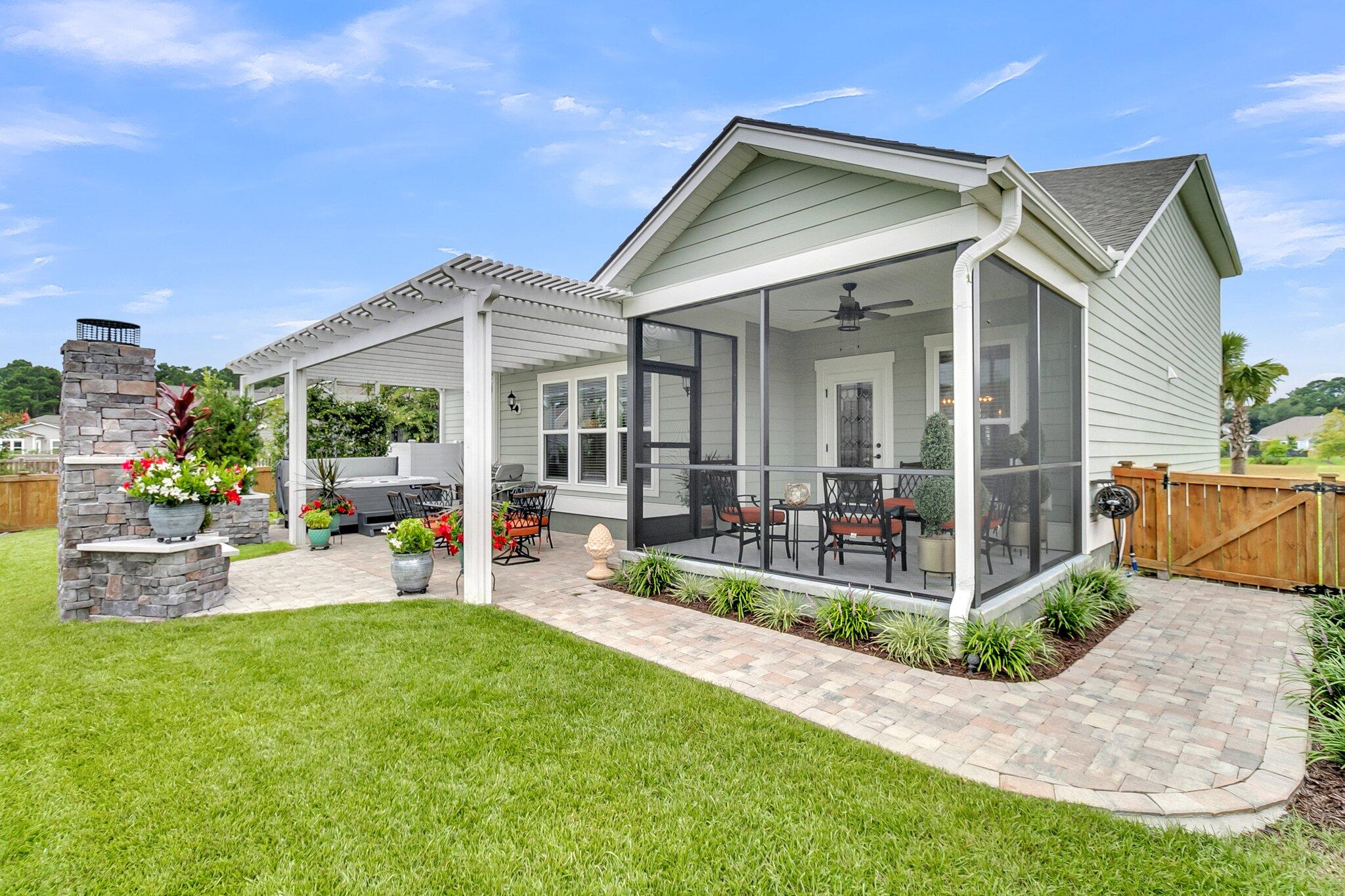 Rear exterior of a home with a screened porch, pergola, paver patio, and stone fireplace.