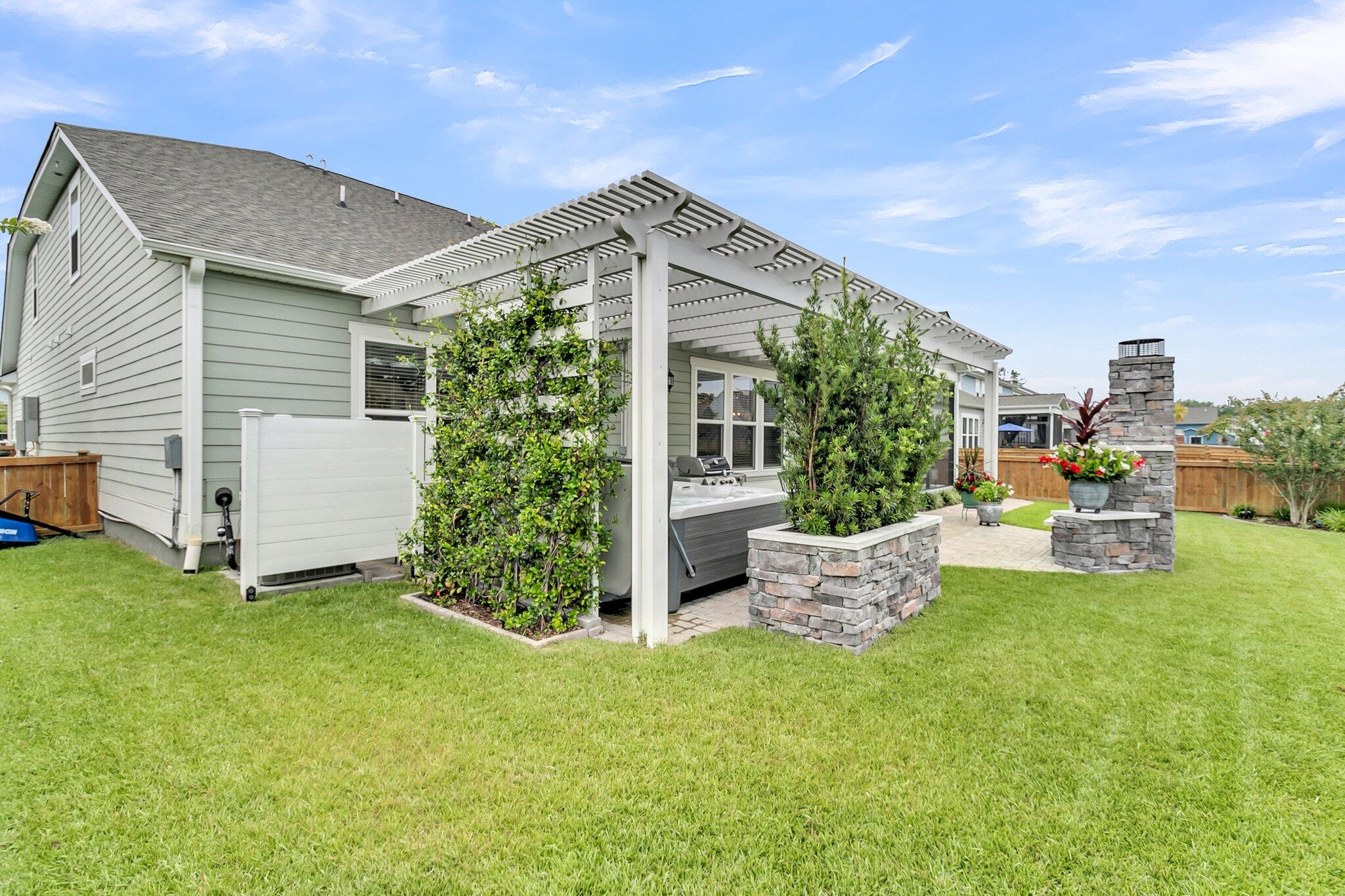 House backyard with a pergola-covered hot tub, stone fireplace, planters, and lawn.