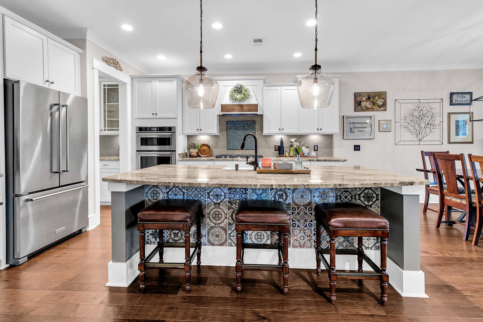 Kitchen with a large island faced in colorful patterned tile and three leather bar stools.