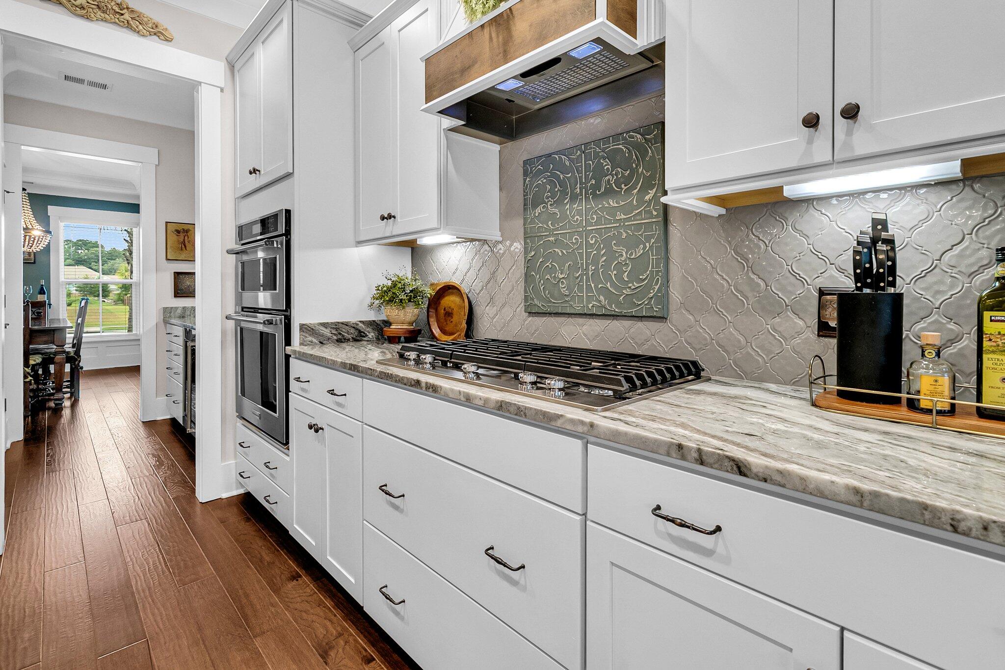 Kitchen with white cabinets, marble counters, a wide gas cooktop, and ornate tile backsplash.