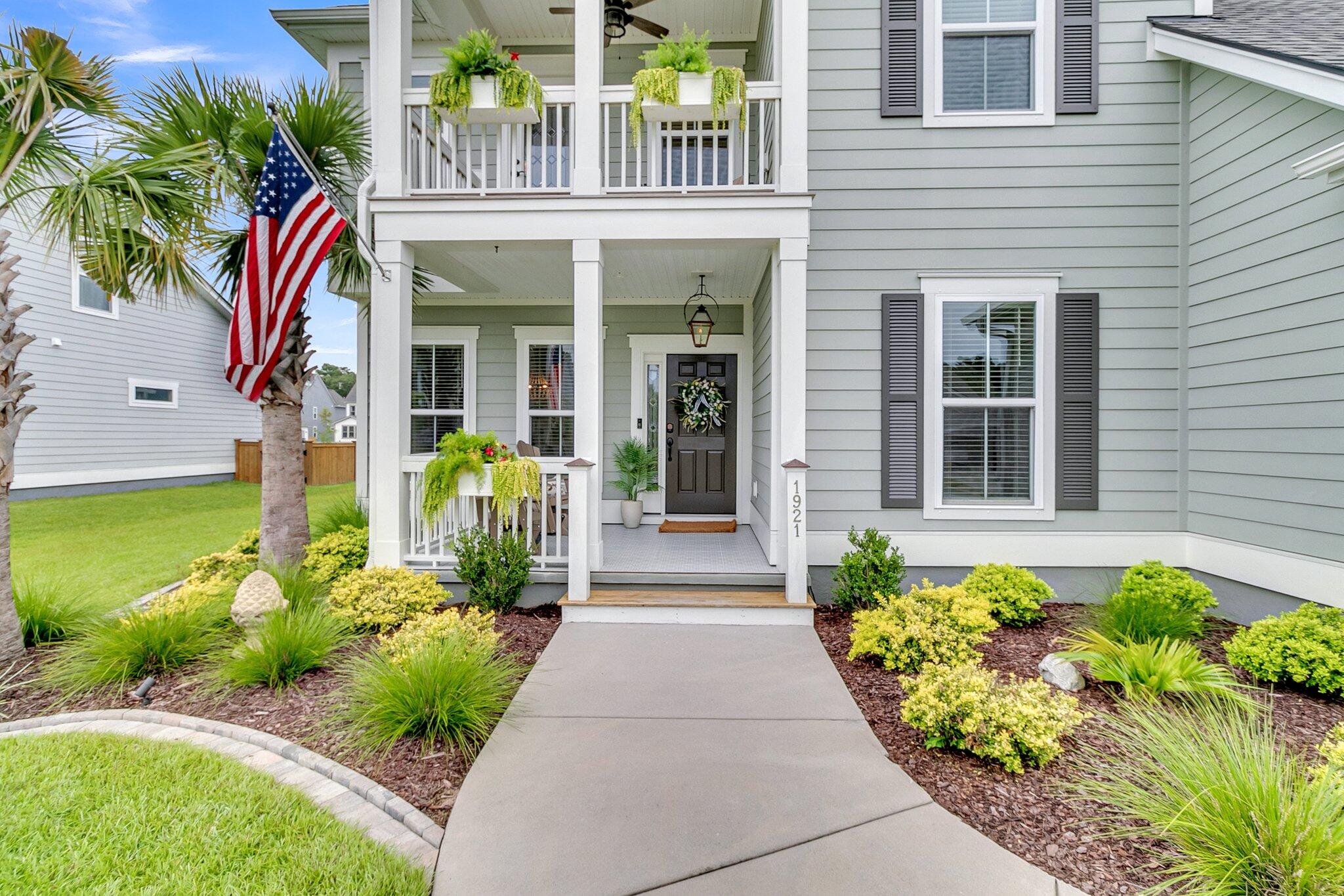 Gray two-story home with a covered porch, hanging plants, and an American flag beside the walkway.