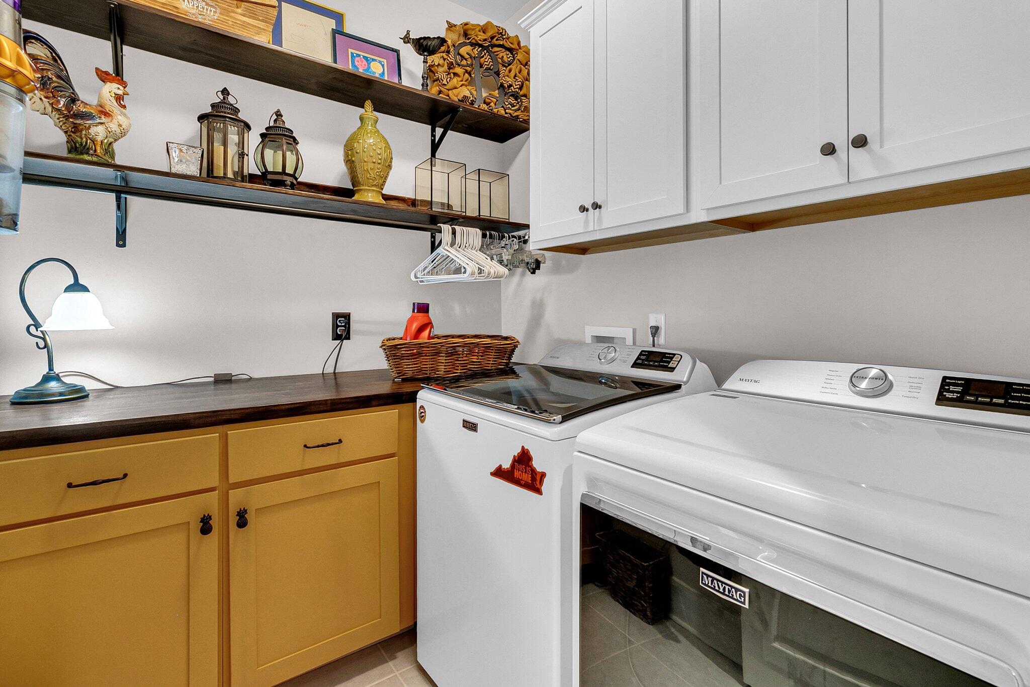 Laundry room with Maytag washer and dryer, mustard-yellow cabinets, and decorative open shelving.