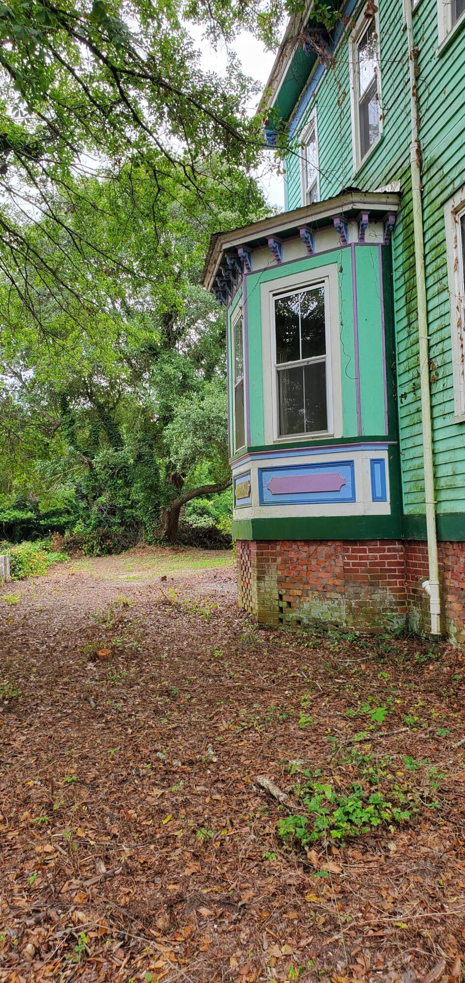 Green house with a colorful projecting bay window beside a leaf-covered yard and mature trees.