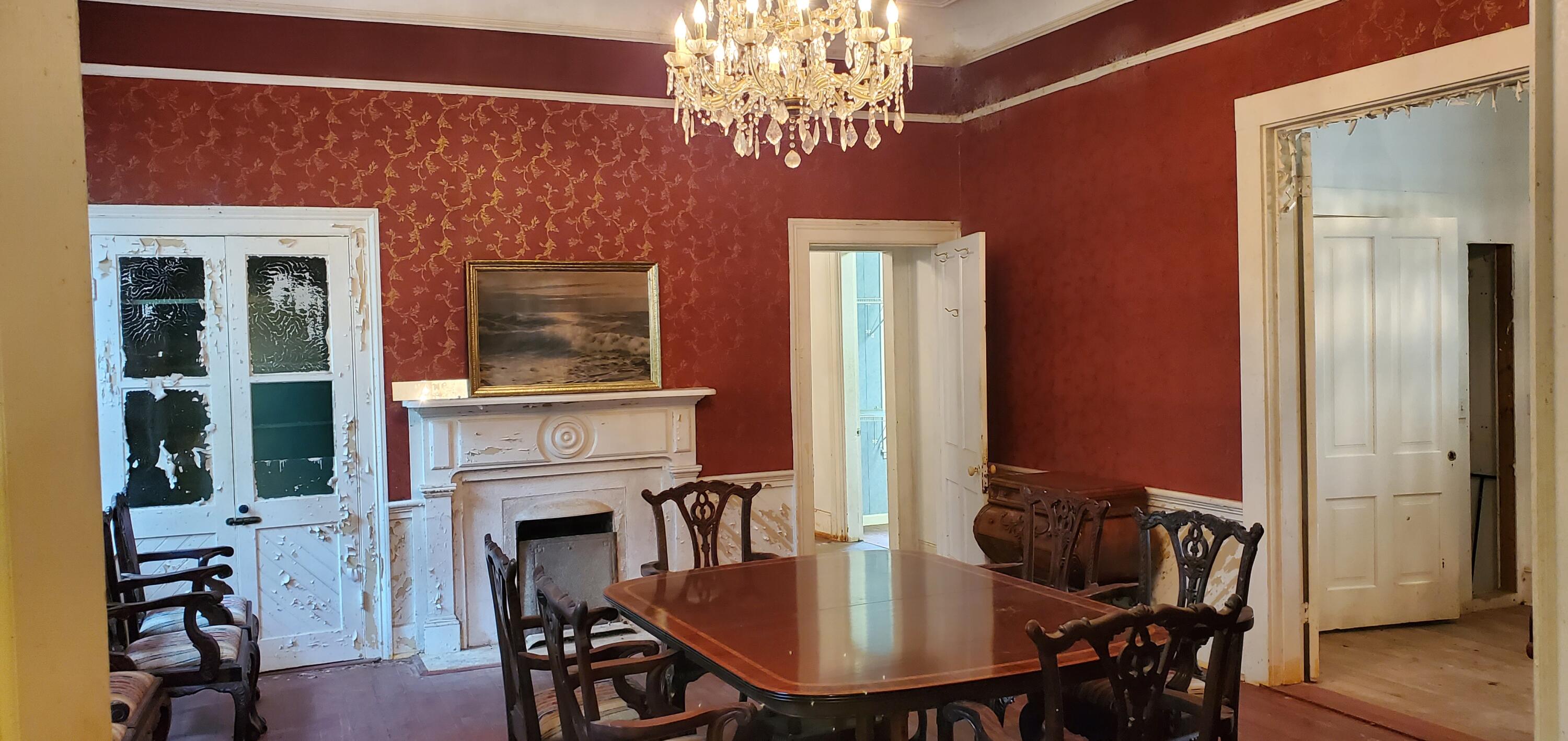Dining room with a crystal chandelier, ornate fireplace, red walls, and carved wooden chairs.