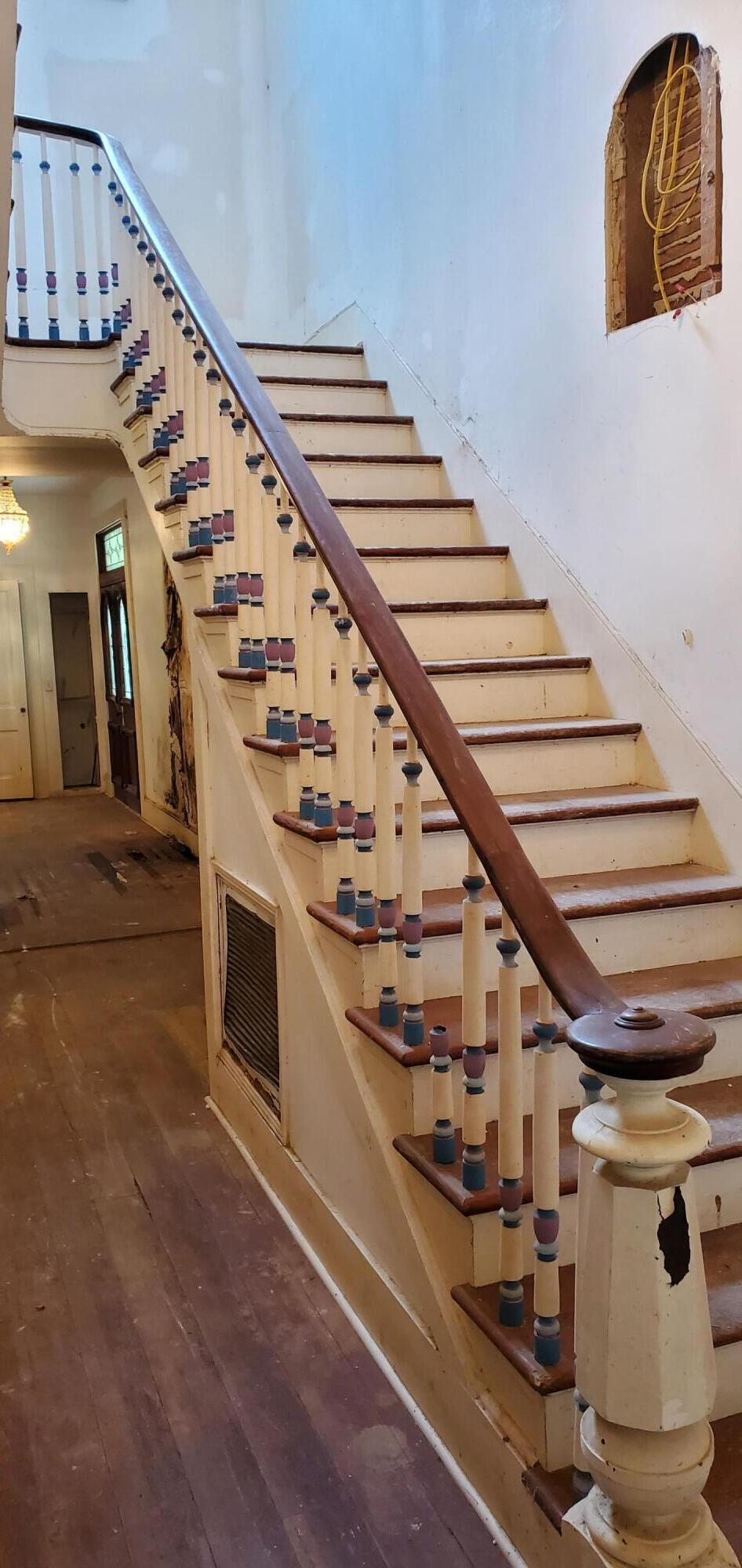 Interior staircase with cream balusters, dark wood rails, and visibly worn floors and walls.