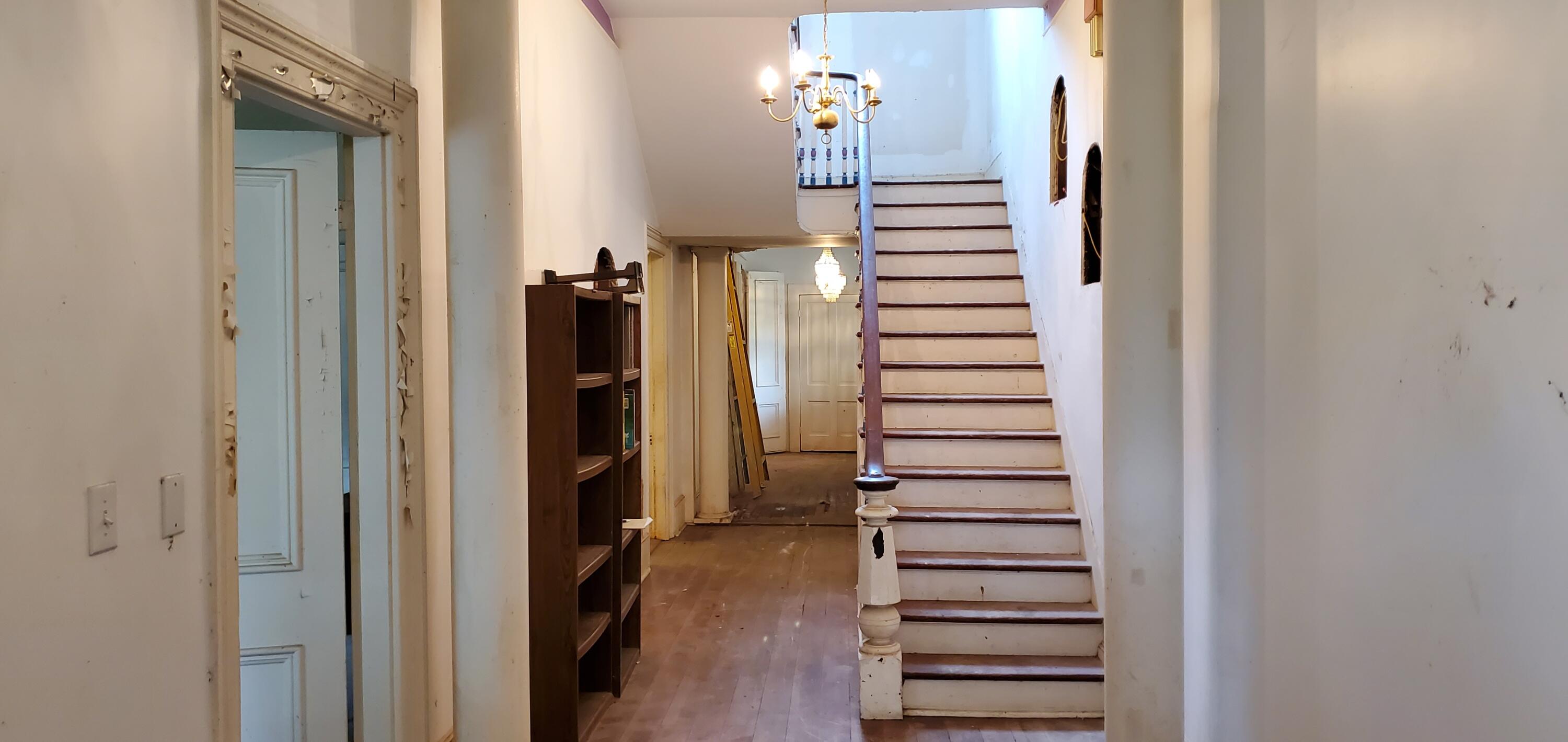 Hallway with a worn wooden staircase, chandelier, hardwood floor, and built-in shelving.