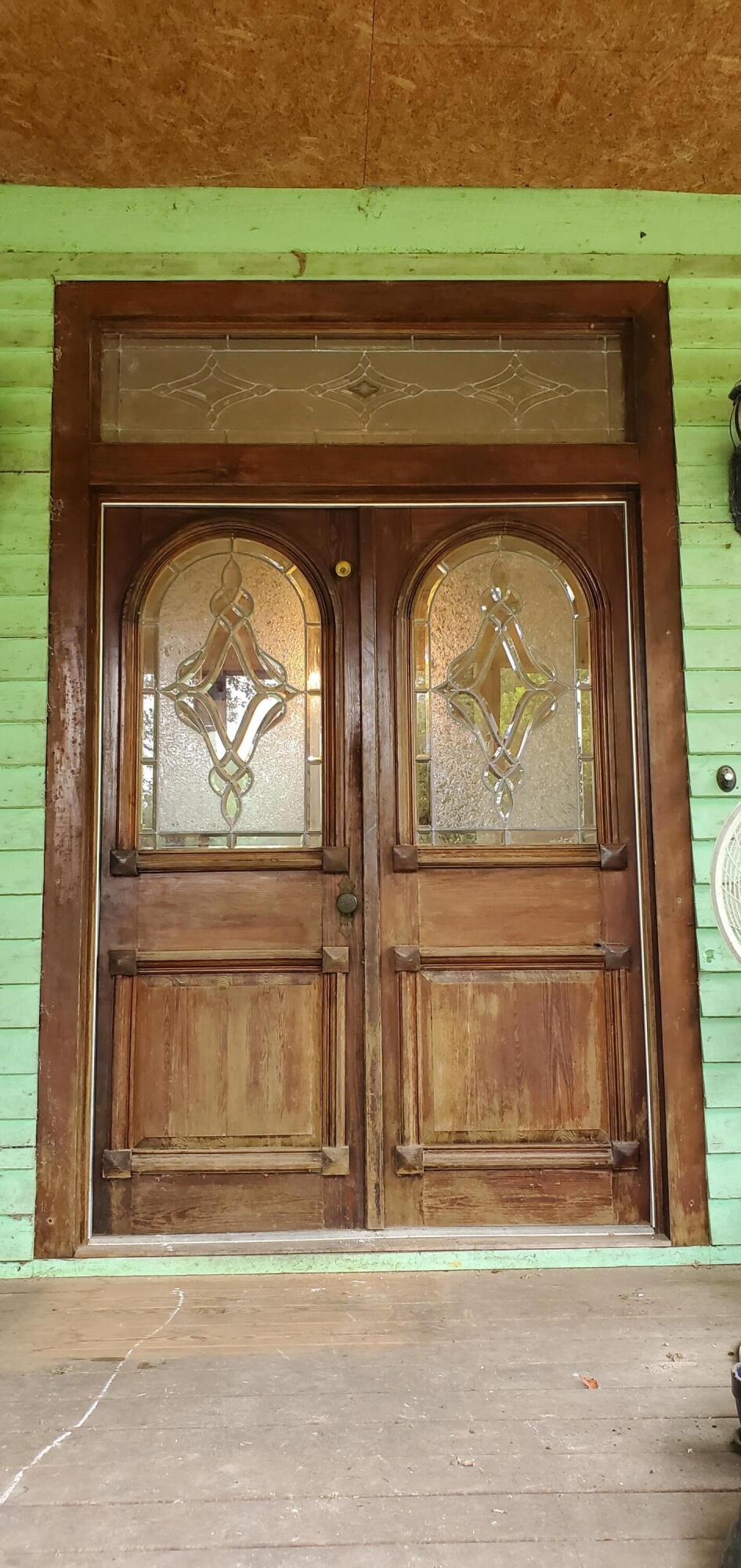 Front entrance with weathered wooden double doors and ornate stained-glass panels in mint-green siding.