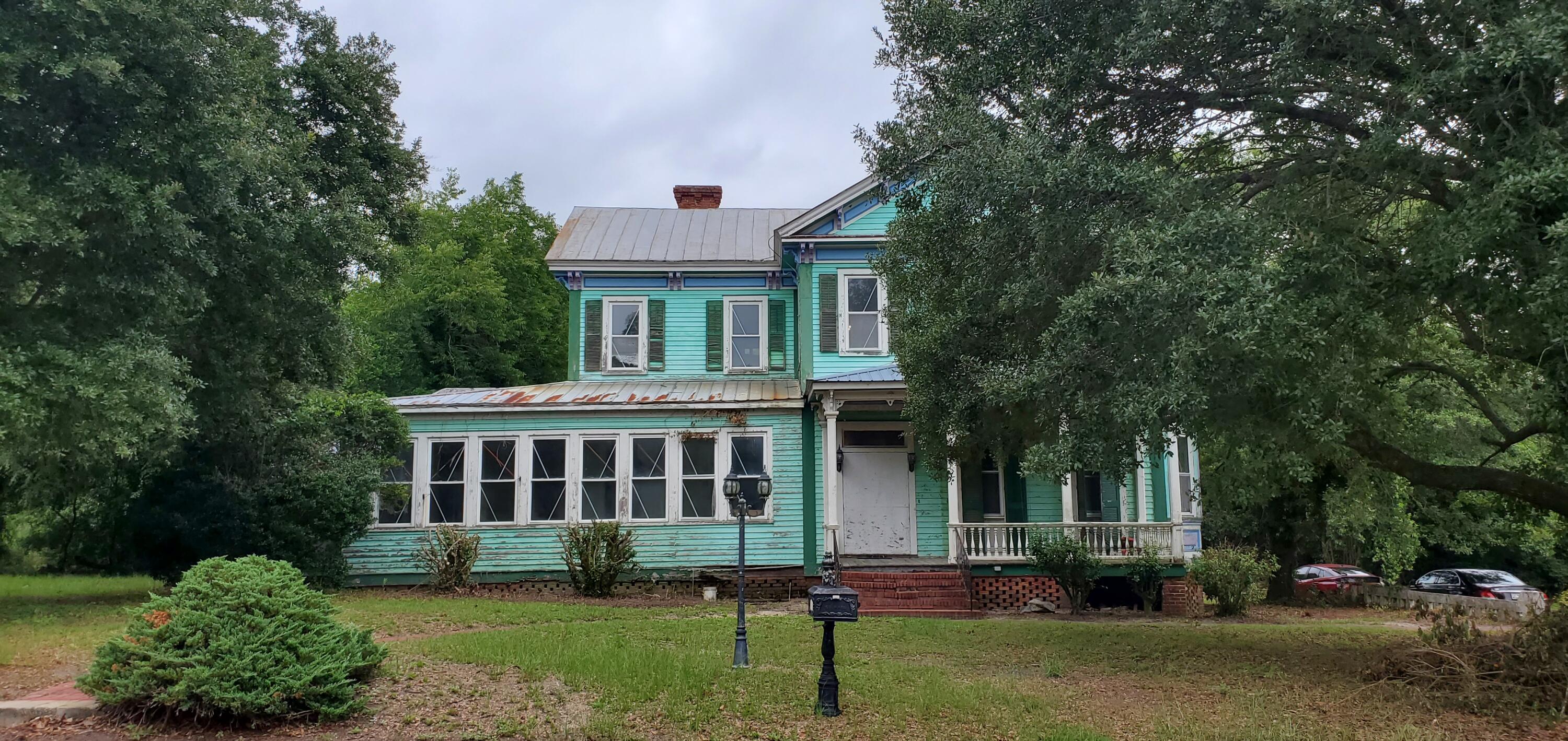 Turquoise two-story house with a weathered metal roof, covered porch, and mature trees.