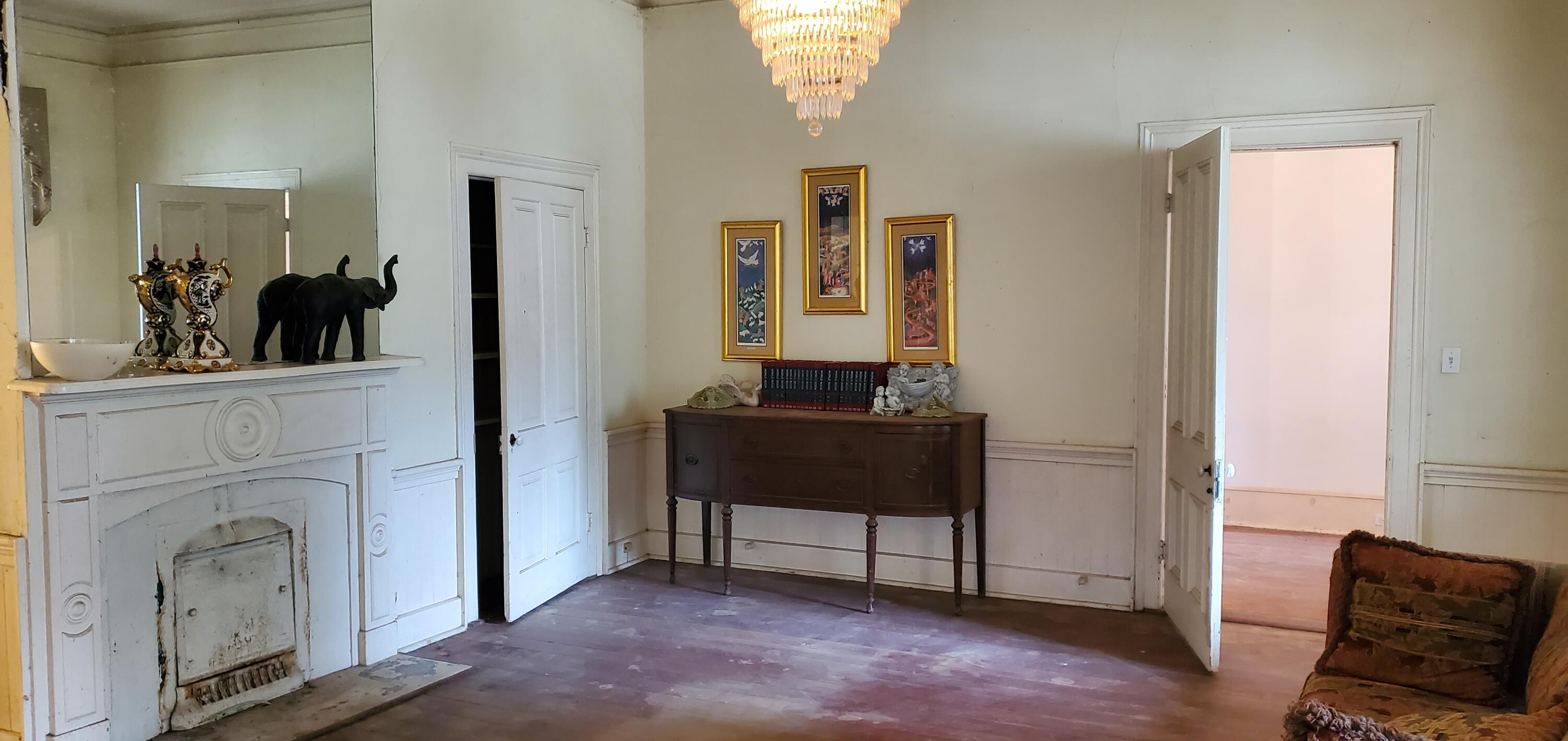 Furnished room with a white fireplace, antique sideboard, chandelier, and worn hardwood floors.