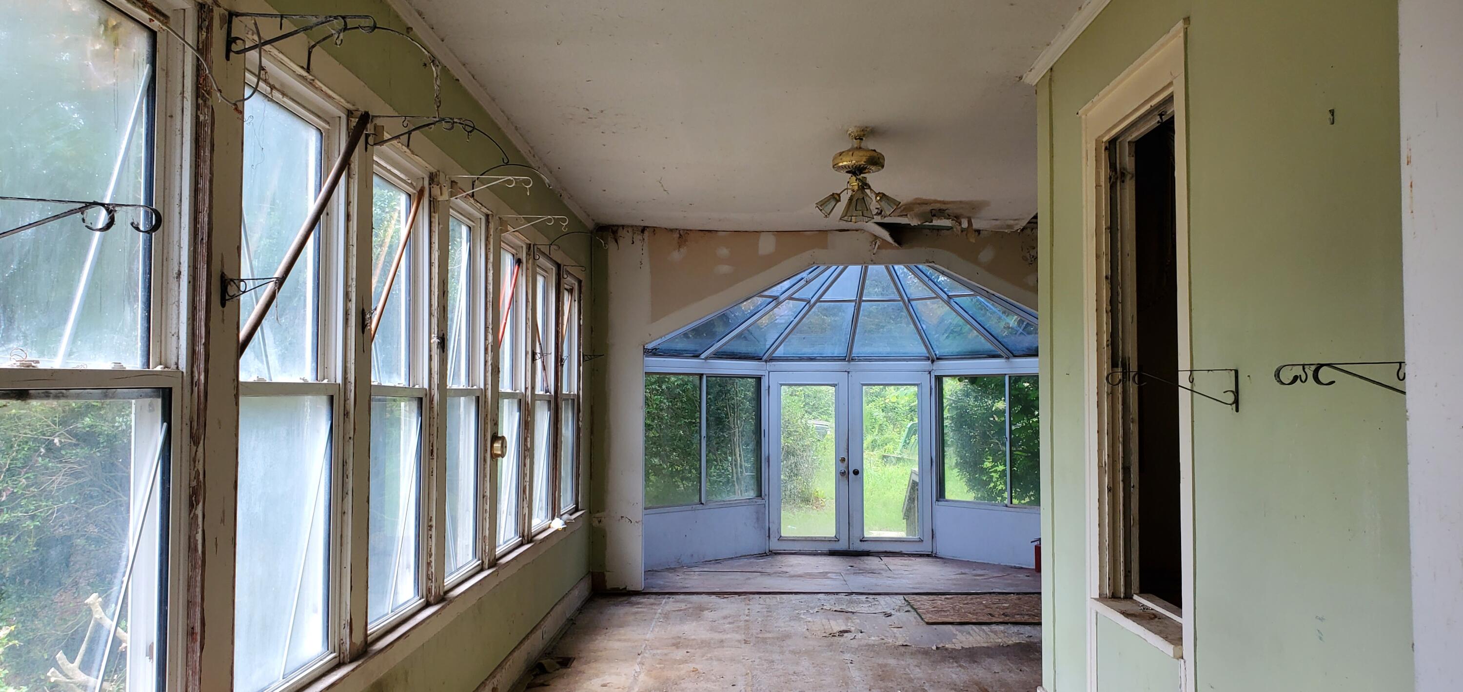 Sunroom with rows of windows, a glass-roofed bay, and a worn floor.