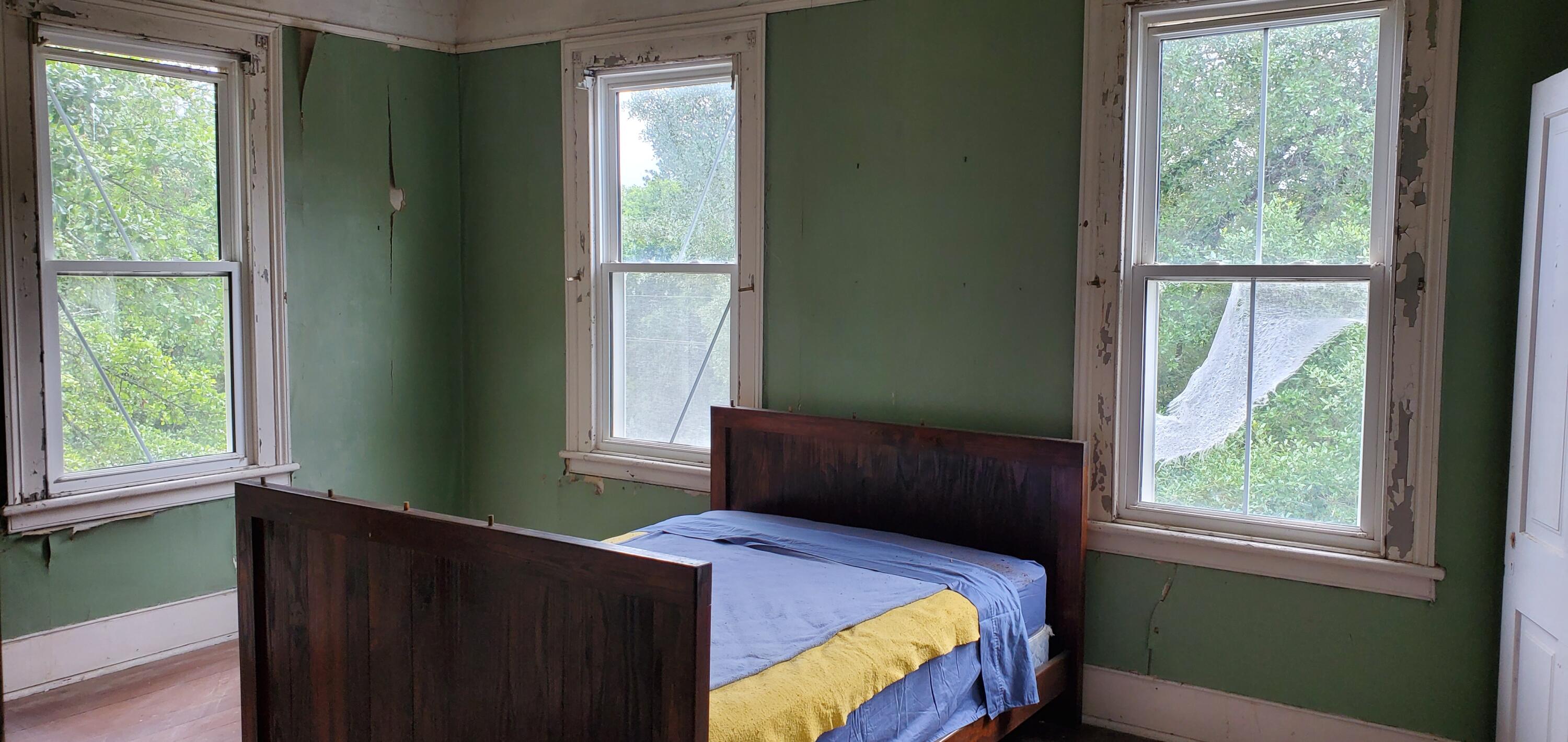 Bedroom with a dark wooden bed, blue and yellow bedding, green walls, and three tall windows.