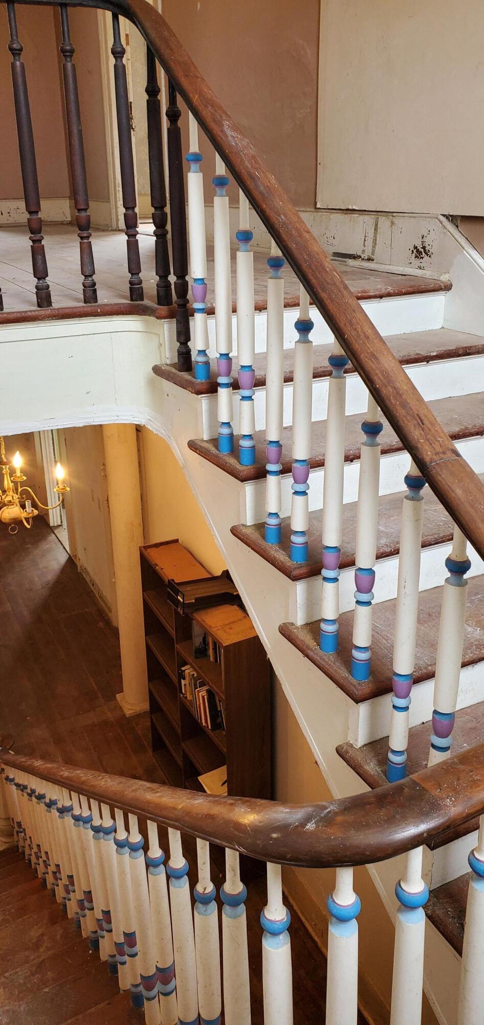 Staircase with blue-and-purple accents on white balusters and worn dark wood handrails.