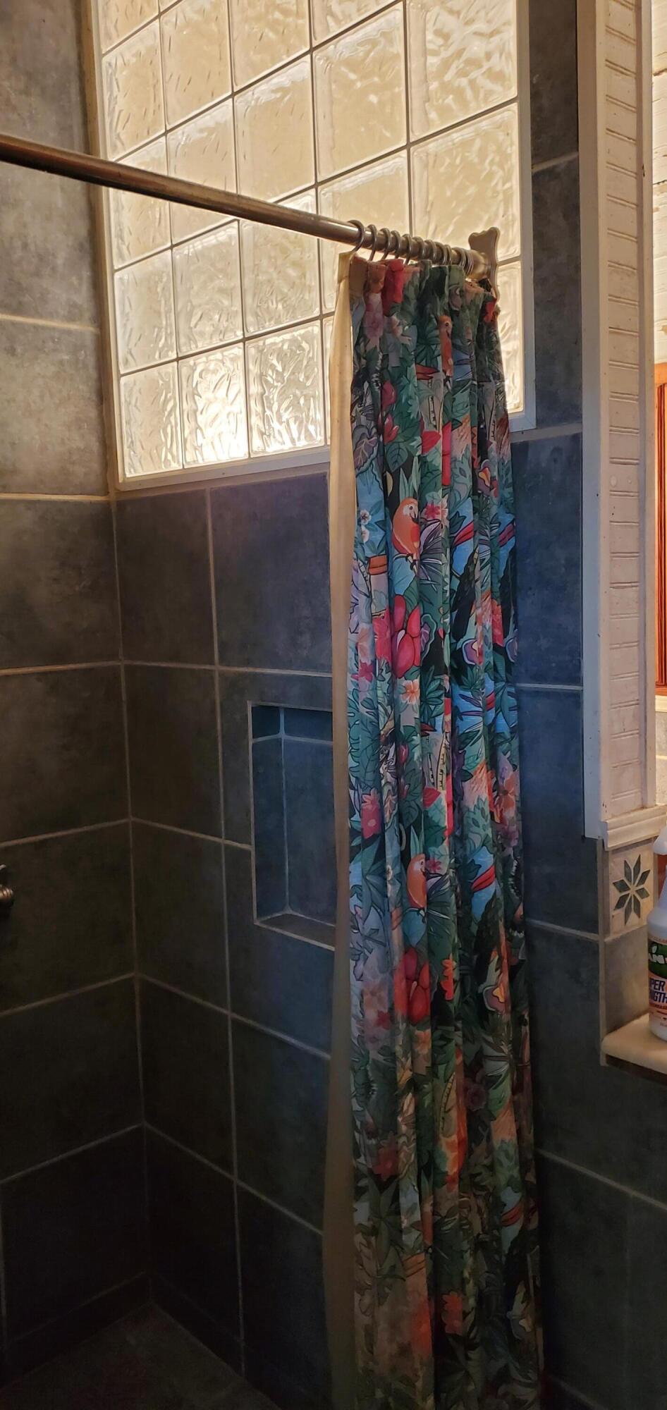 Tiled shower with glass block windows and a colorful tropical-print curtain.