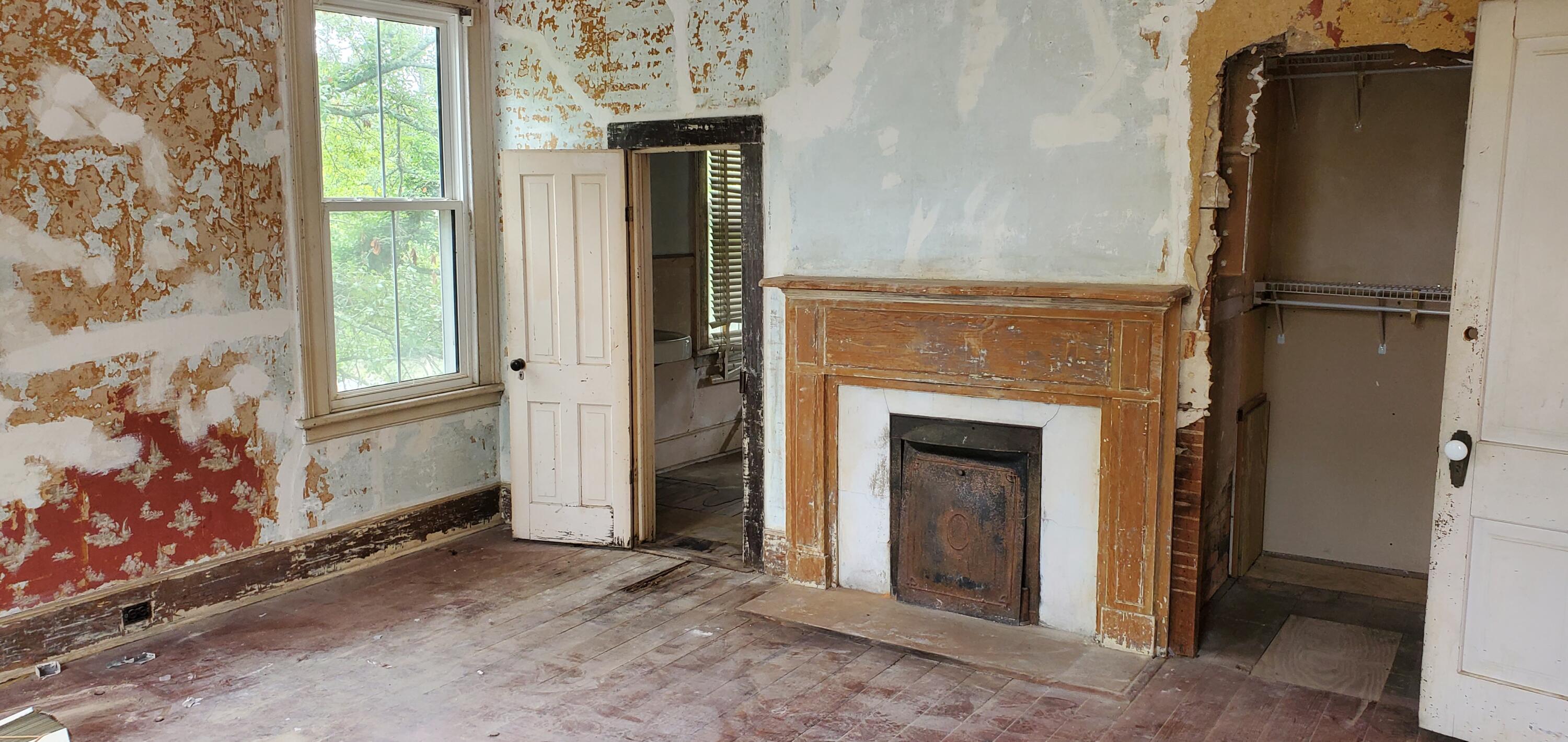Unfinished room with a weathered fireplace mantel, peeling walls, and an open closet.