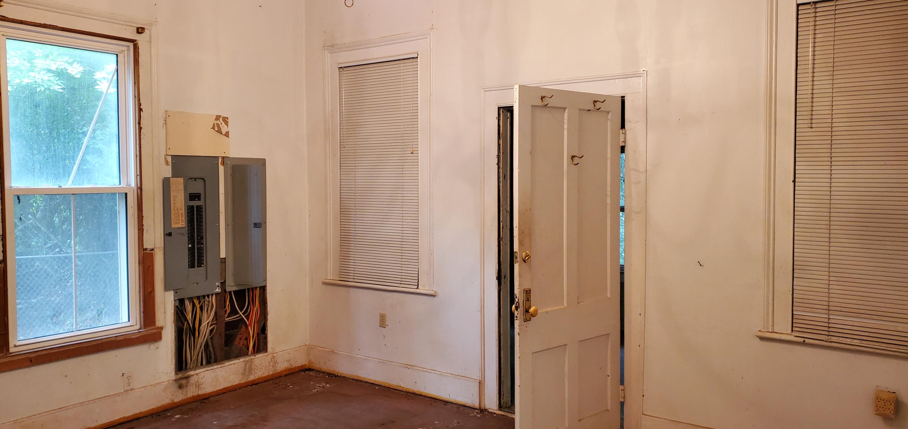 Vacant room with exposed electrical wiring, two windows, and an open door.