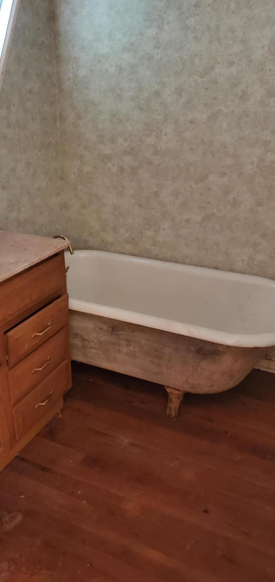 Bathroom with a white clawfoot tub, brass faucet, and wooden vanity.
