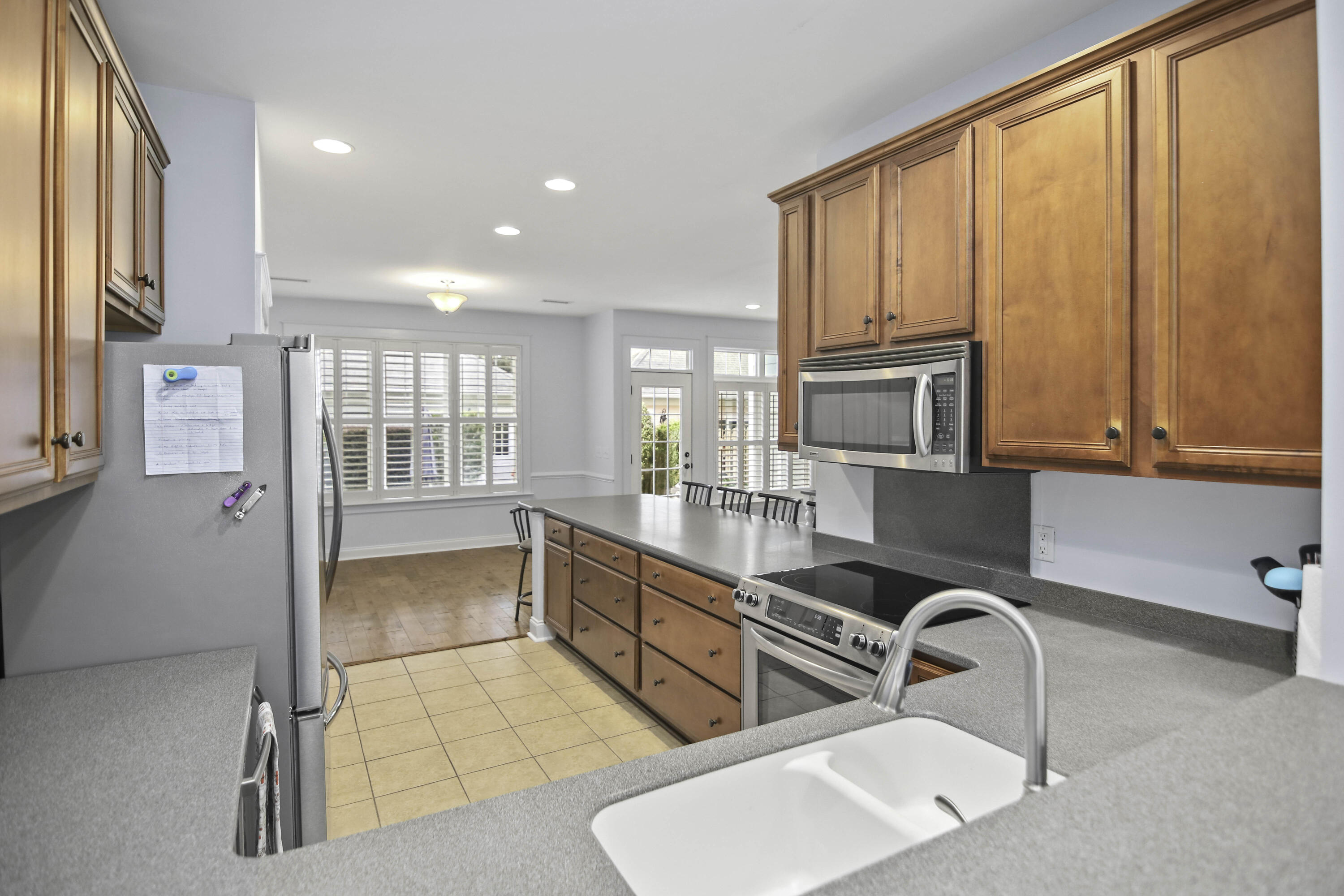 Kitchen with warm wood cabinetry, stainless steel appliances, gray counters, and shuttered windows.