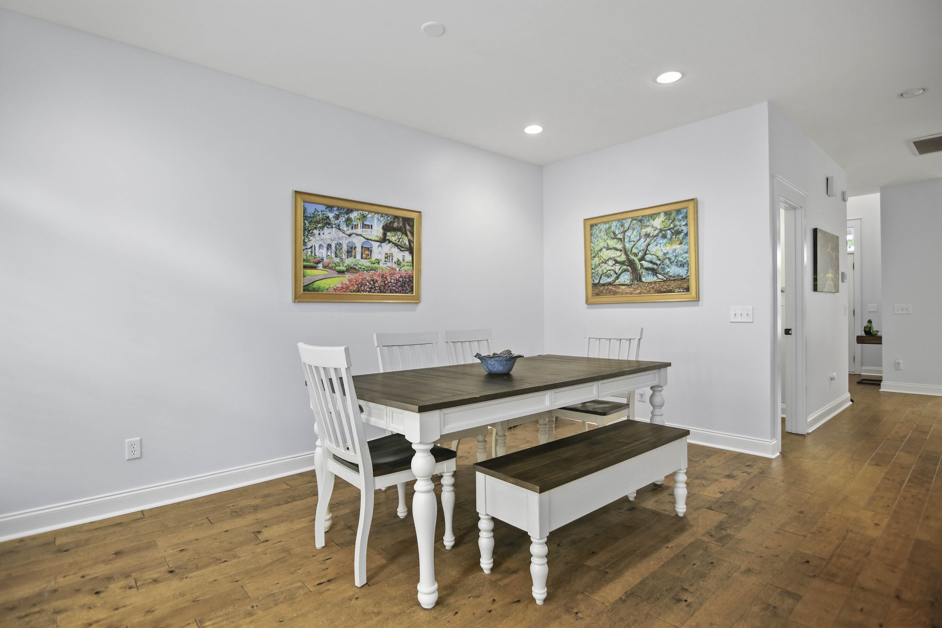 Dining area with a white table, dark wood top, matching chairs, and warm wood flooring.
