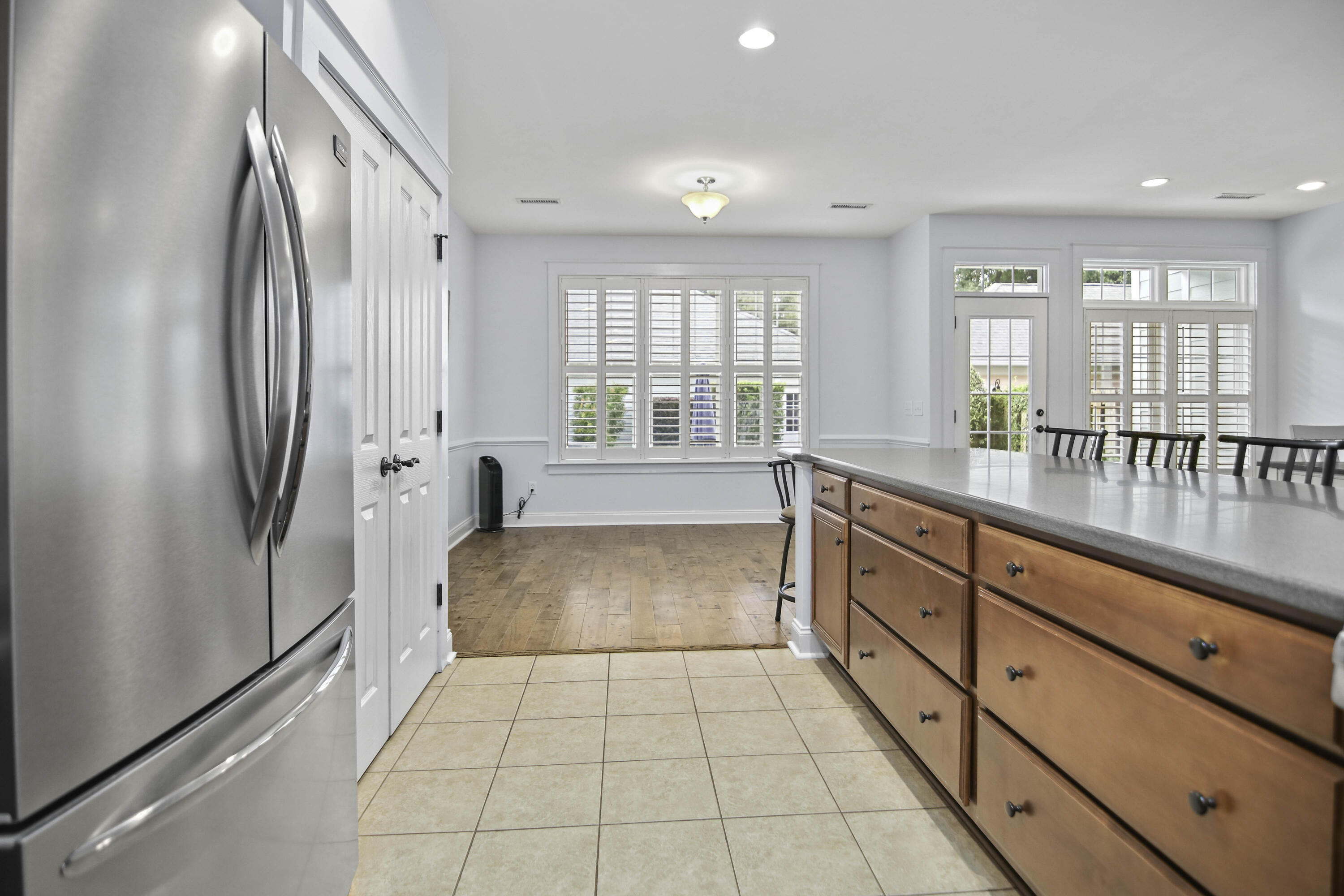 Bright kitchen with a long wood island, stainless refrigerator, and shuttered windows and doors.