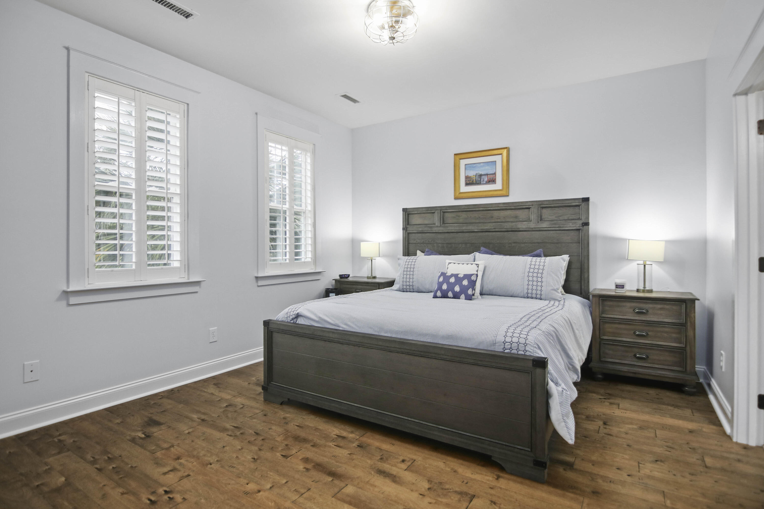 Bedroom with a dark wood bed, blue-and-white bedding, plantation shutters, and wood floors.