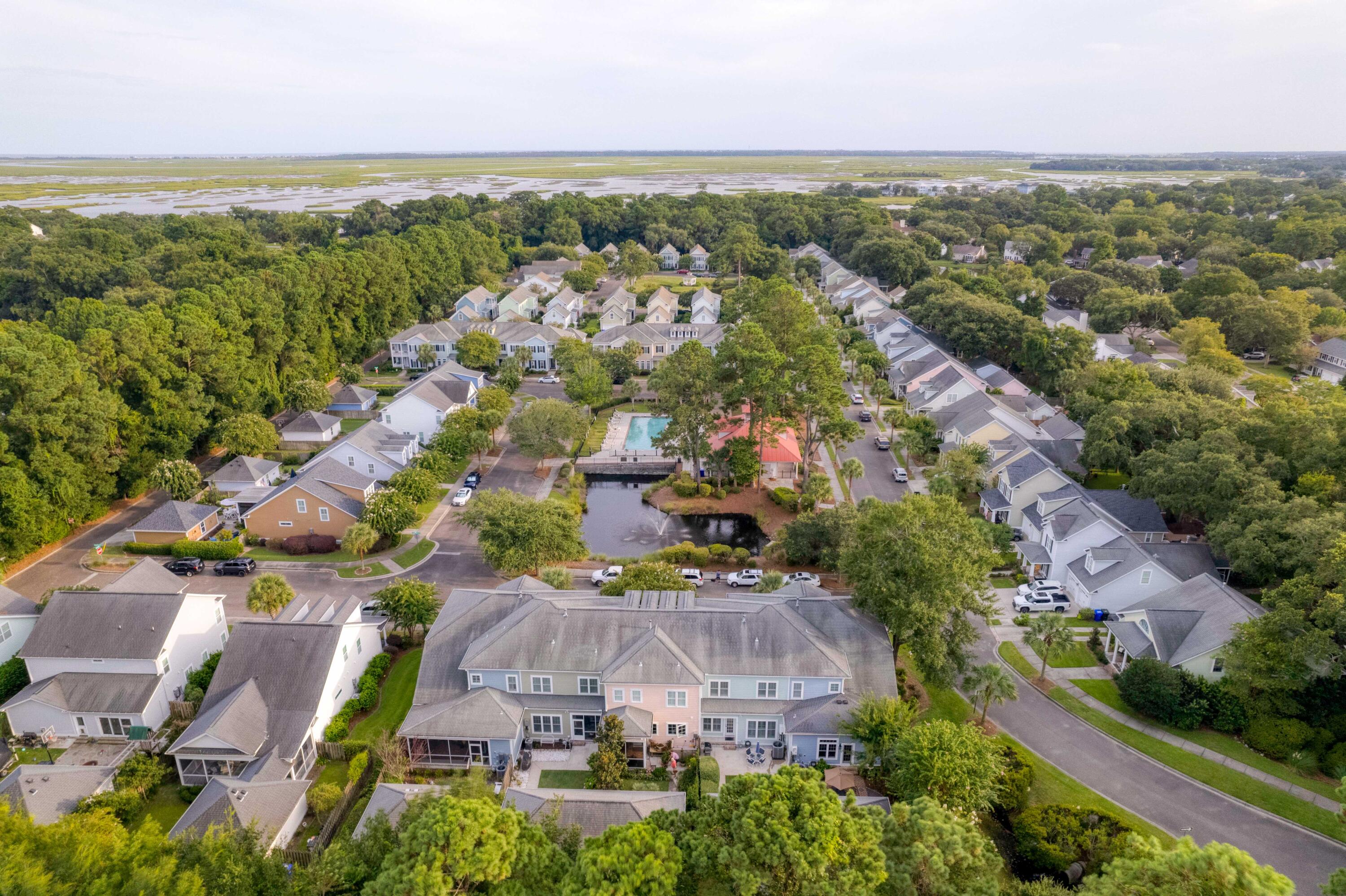Aerial view of a tree-lined neighborhood with a community pool, pond, and coastal marshland beyond.