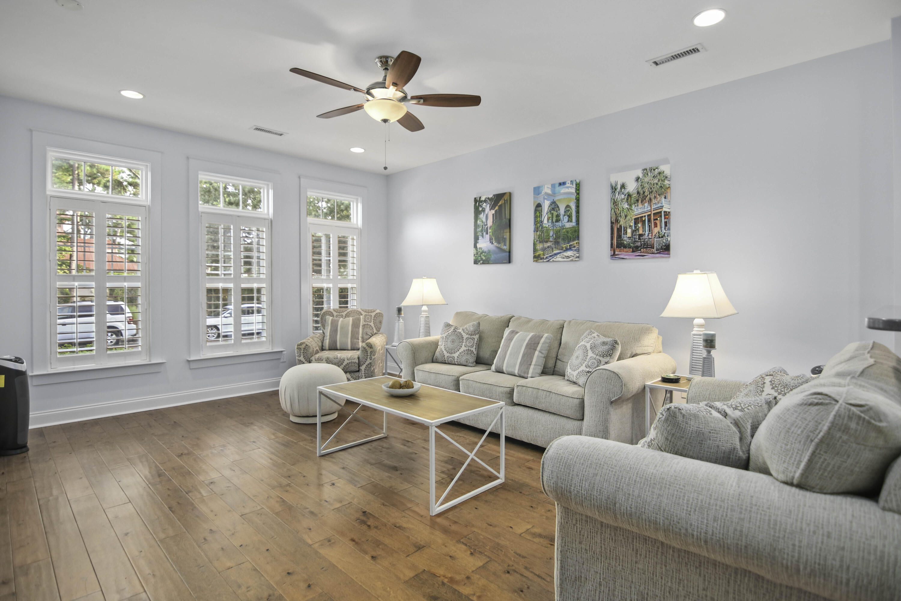 Living room with light sofas, wood floors, shuttered windows, and a ceiling fan.