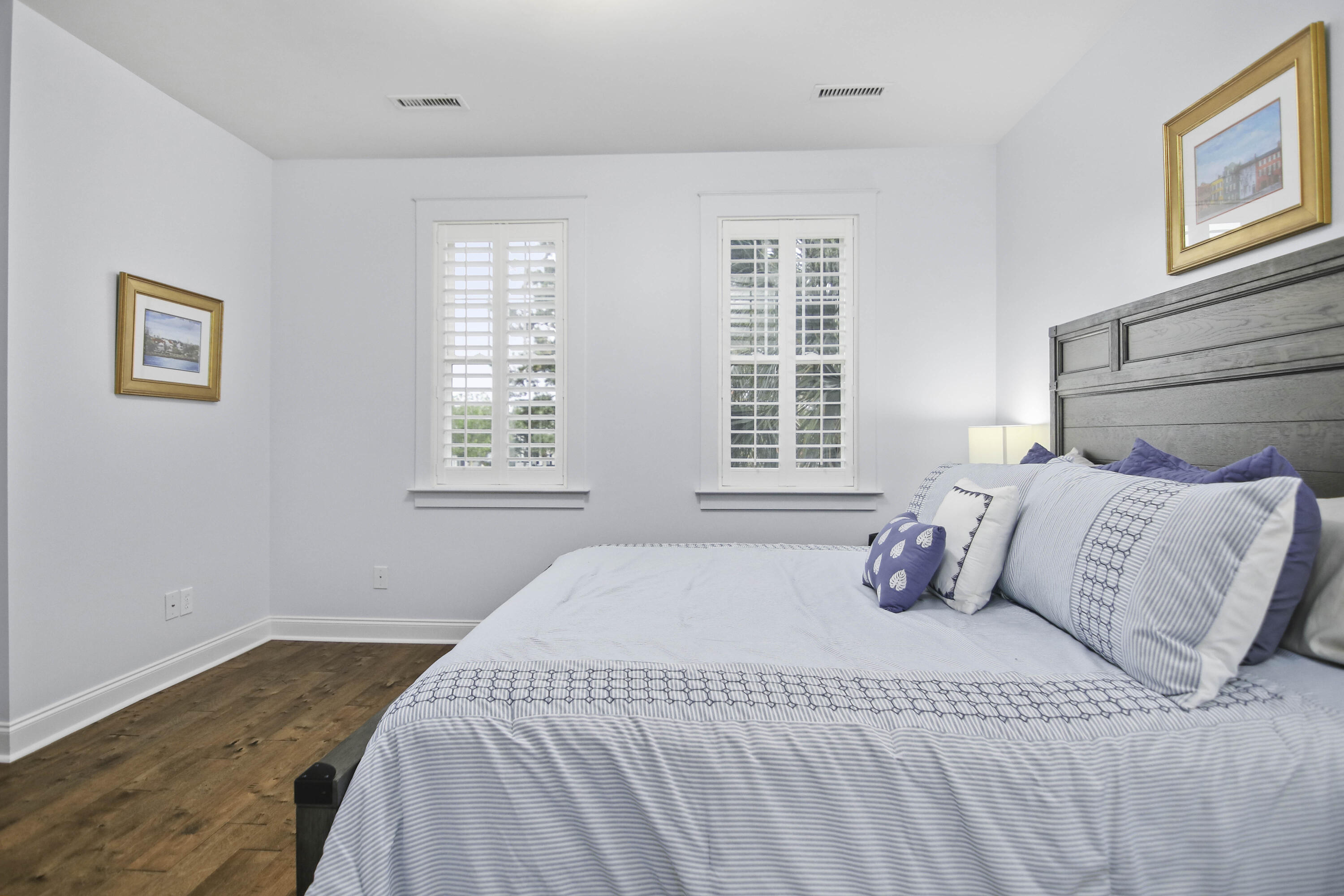 Furnished bedroom with a large pale blue bed, shuttered windows, and warm wood flooring.