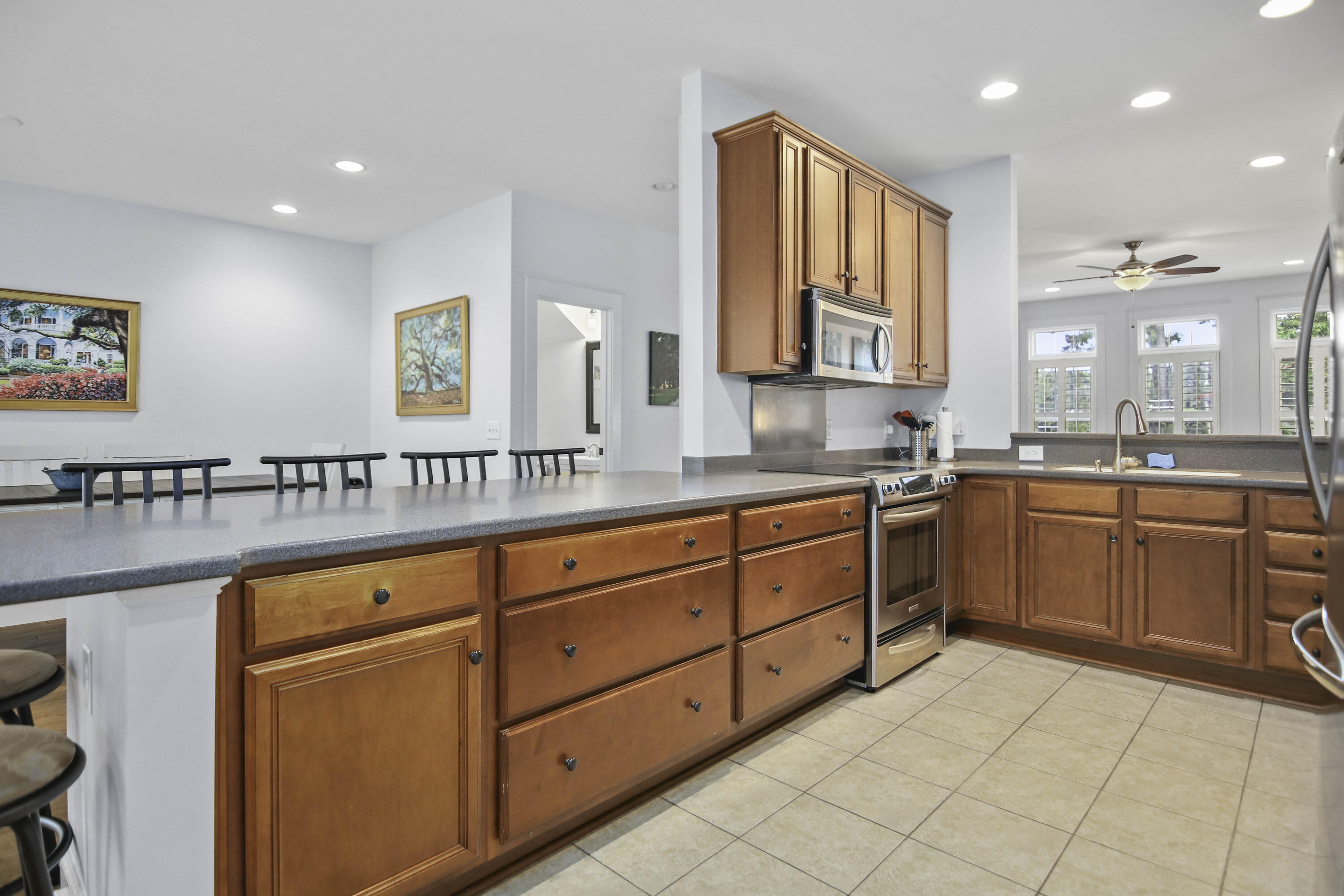 Kitchen with reddish wood cabinetry, a long breakfast bar, stainless appliances, and a sink beneath wide windows.