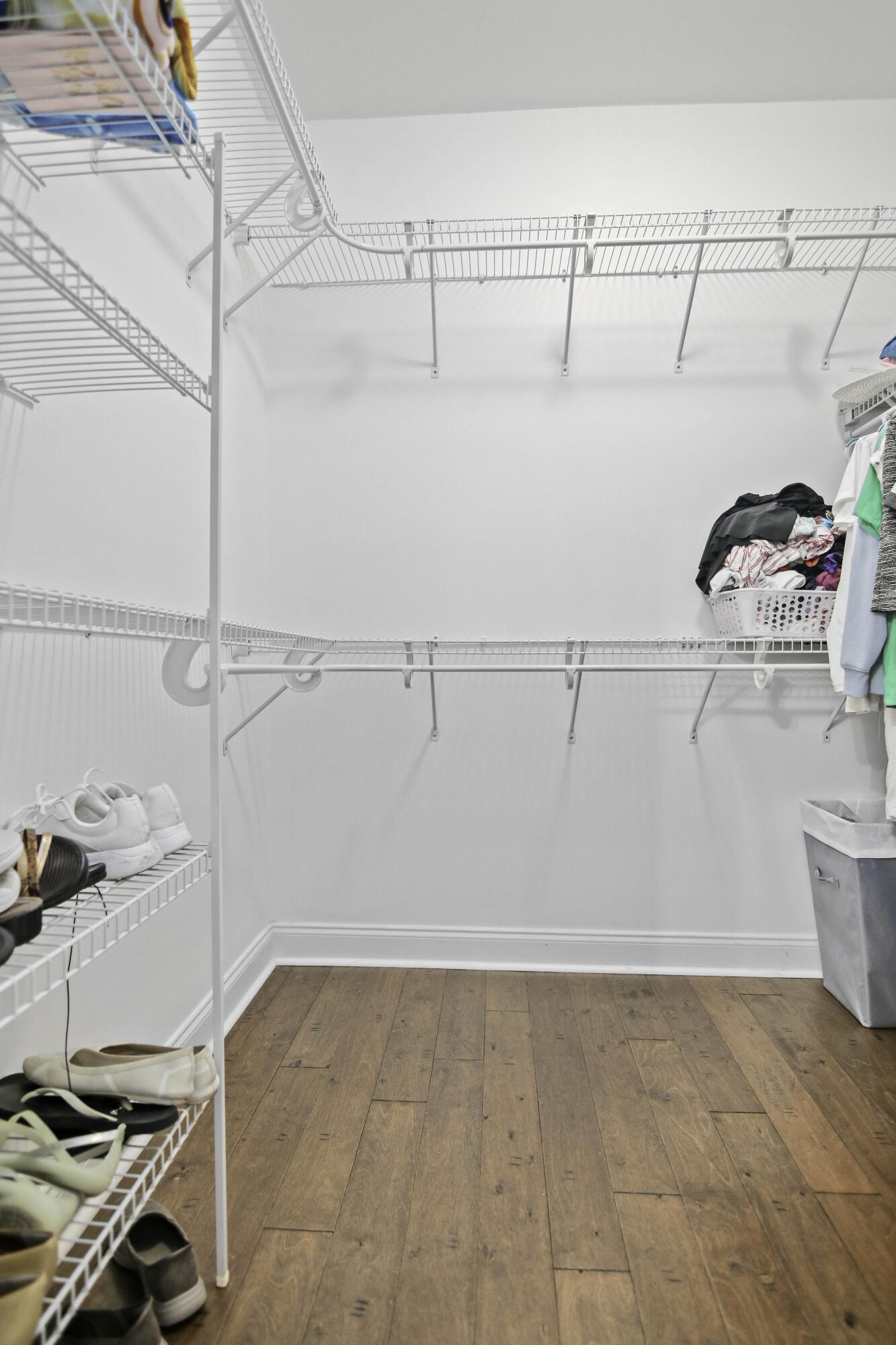 Walk-in closet with white wire shelving, stored shoes and clothes, and wood flooring.