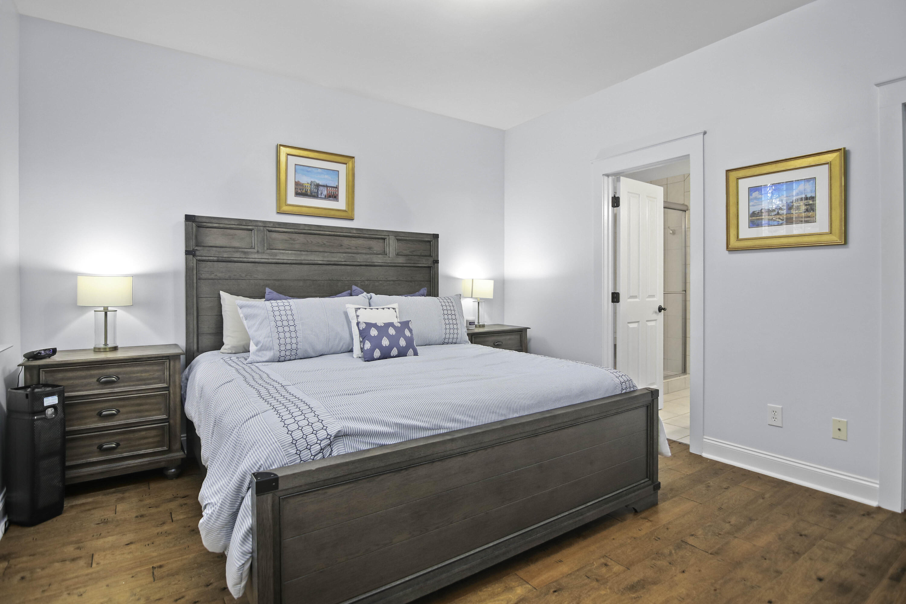 Bedroom with a dark wood bed, blue-and-white bedding, hardwood floors, and an open bathroom doorway.