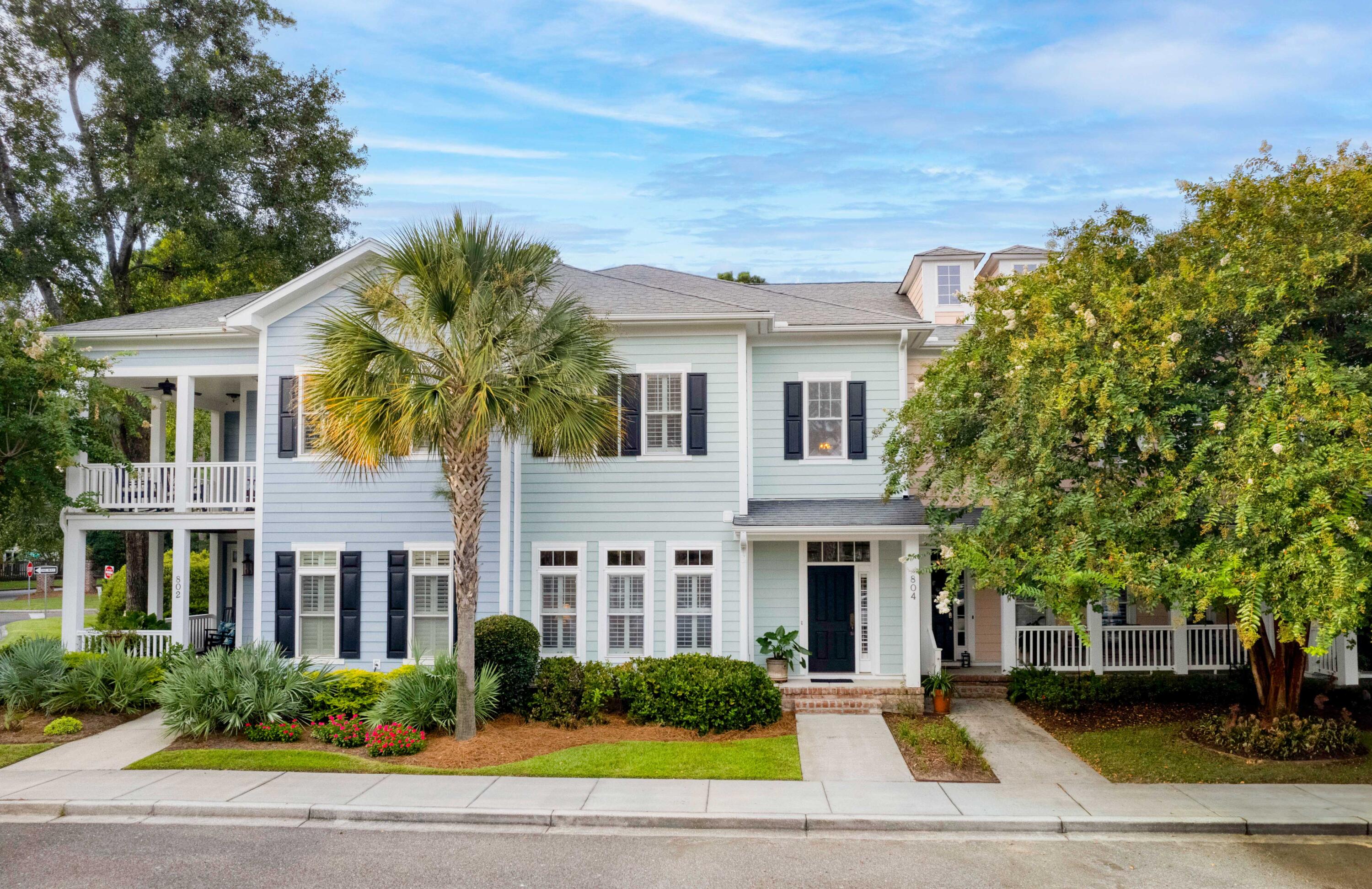 Light blue two-story home with covered porches, dark shutters, and a palm tree in front.