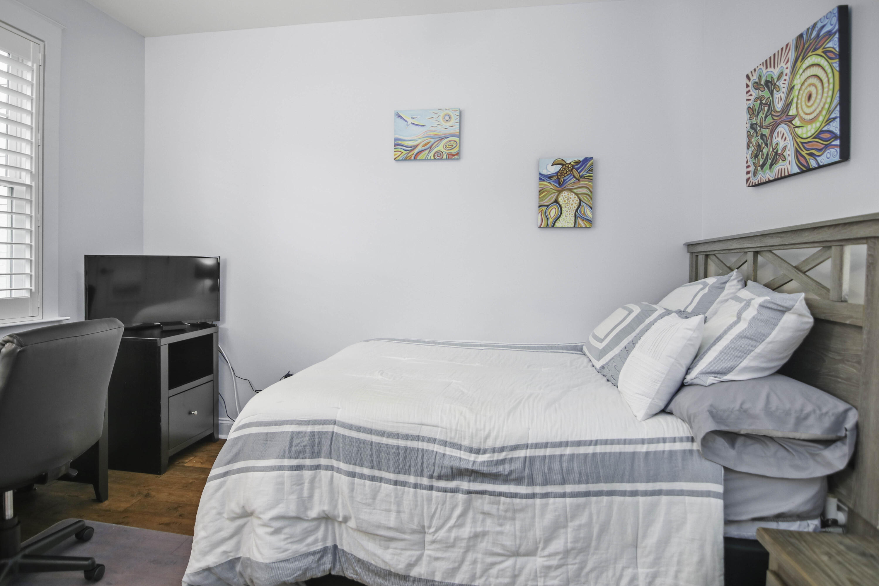 Bedroom with a large striped bed, rustic wood headboard, colorful art, and television.