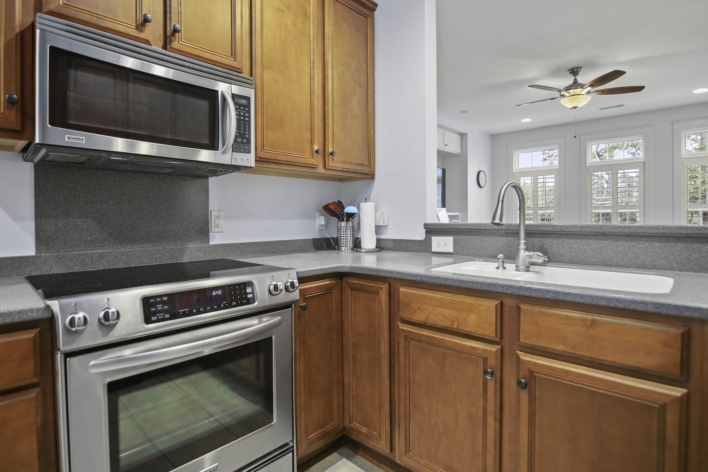 Kitchen with reddish-brown cabinets, stainless steel appliances, gray counters, and a white sink.