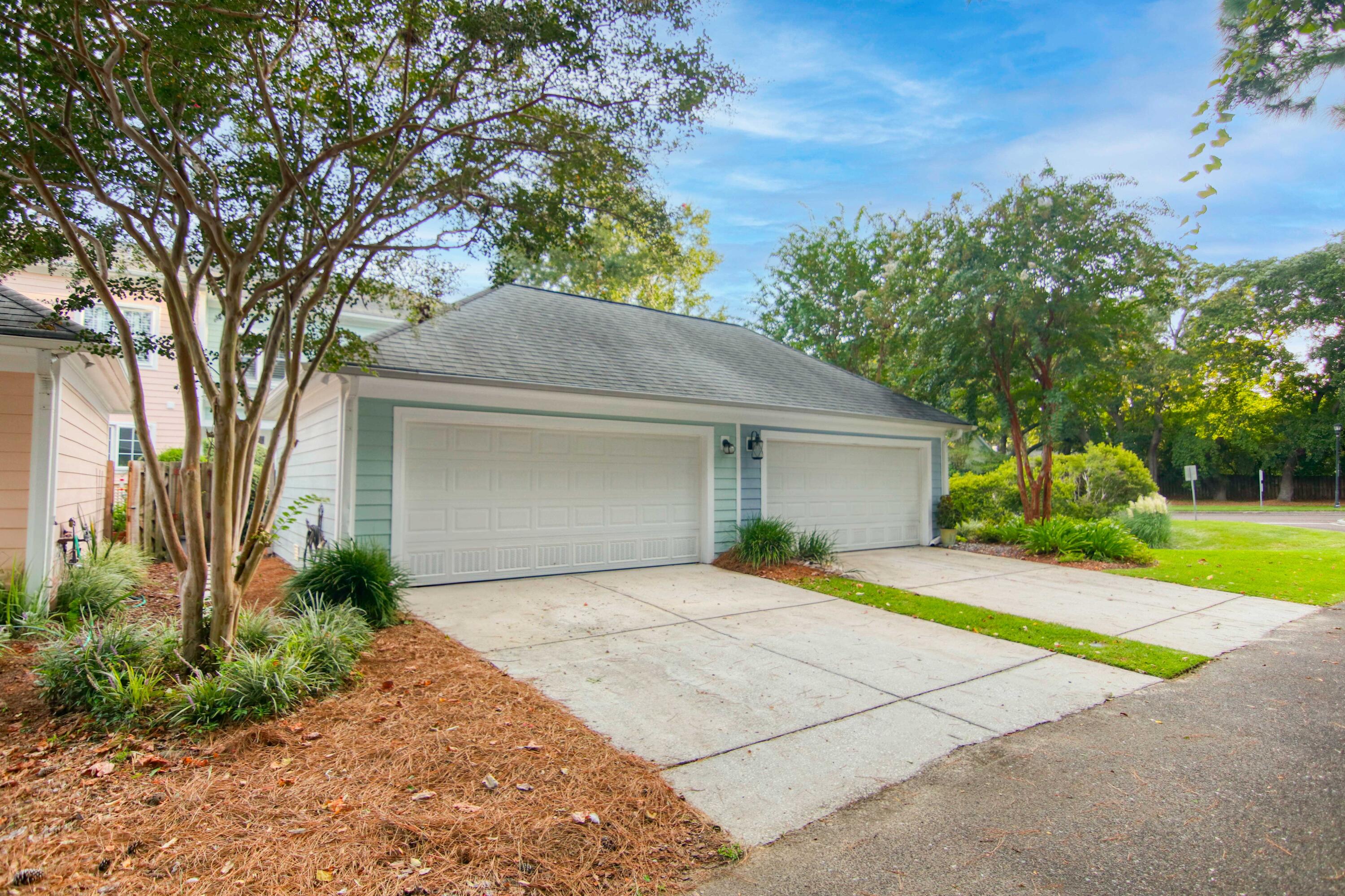 Two-car garage with pale blue-gray siding, white doors, concrete driveways, and mature trees.