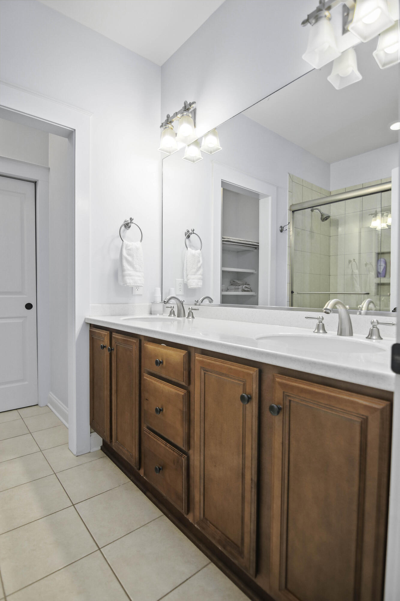 Bathroom with a long double-sink vanity, warm wood cabinets, and a tiled glass shower.