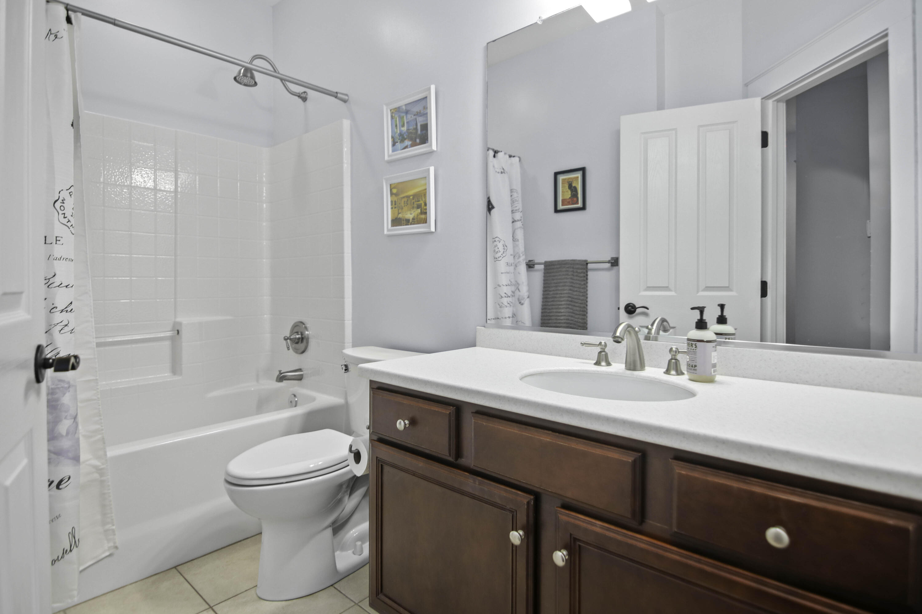 Bathroom with a white tub and shower, toilet, and dark wood vanity with a white countertop.