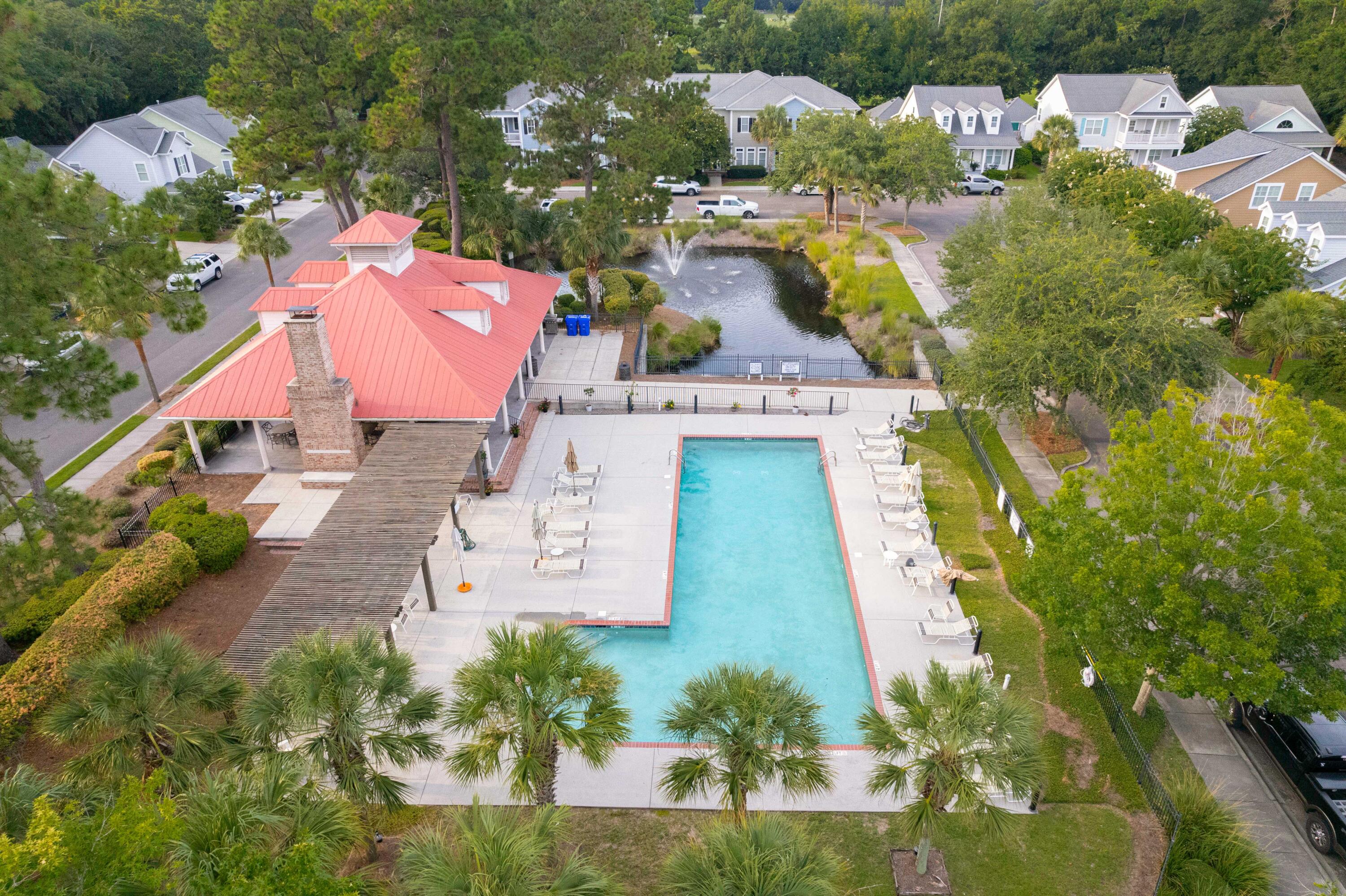 Community swimming pool beside a red-roofed clubhouse and landscaped pond.