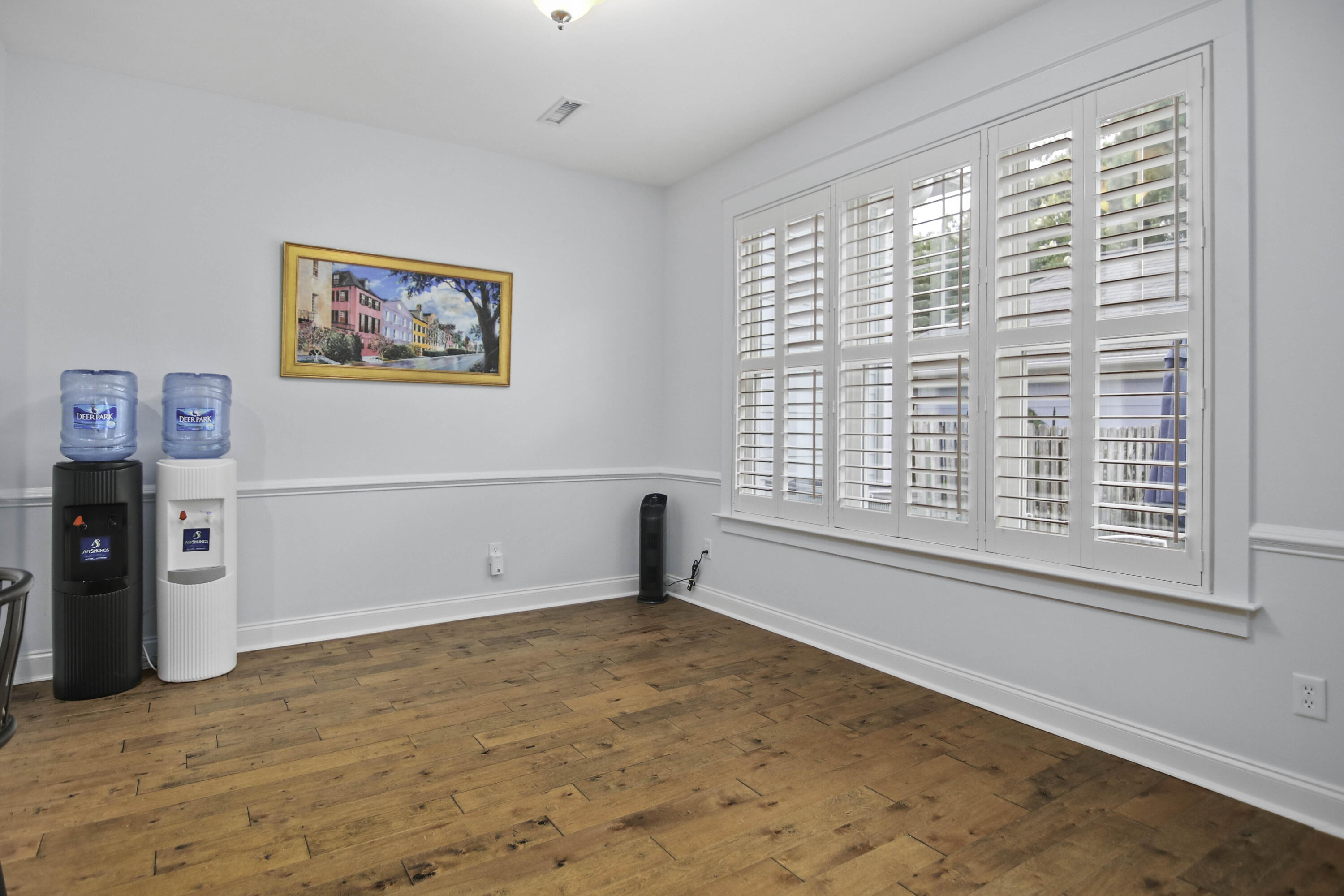 Empty room with wood plank floors, wide plantation shutters, and two water dispensers.