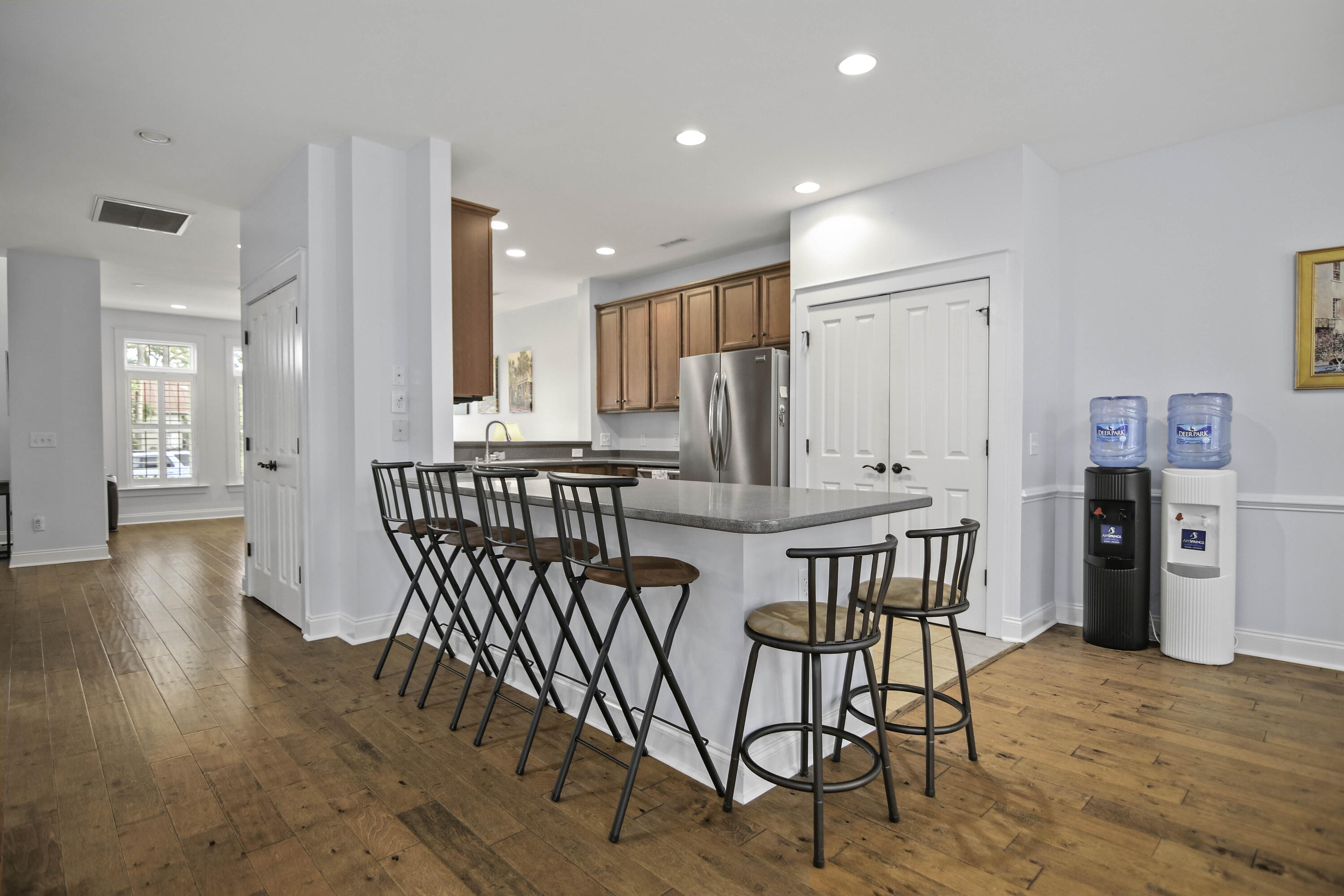 Kitchen with a large stool-lined island, reddish-brown cabinets, stainless refrigerator, and warm wood floors.