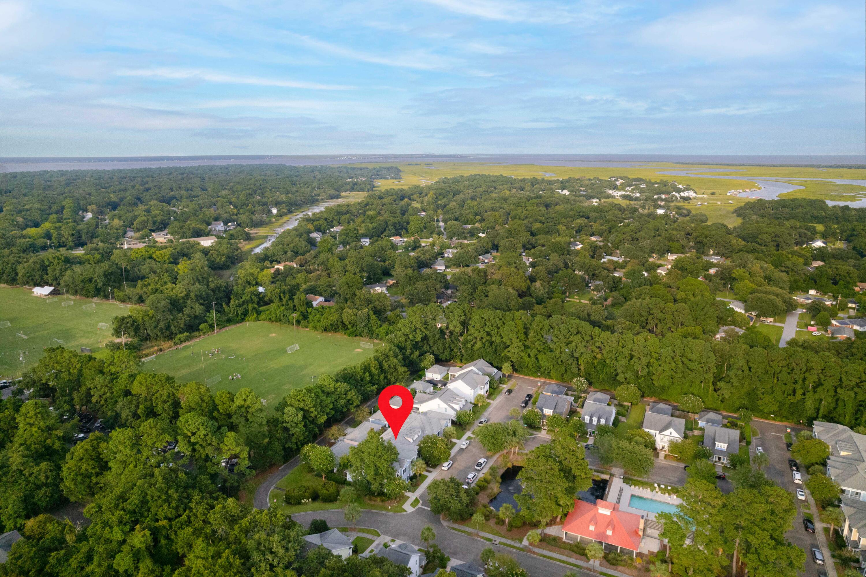 Aerial view of a home marked by a red pin, near a sports field, community pool, and coastal marshland.