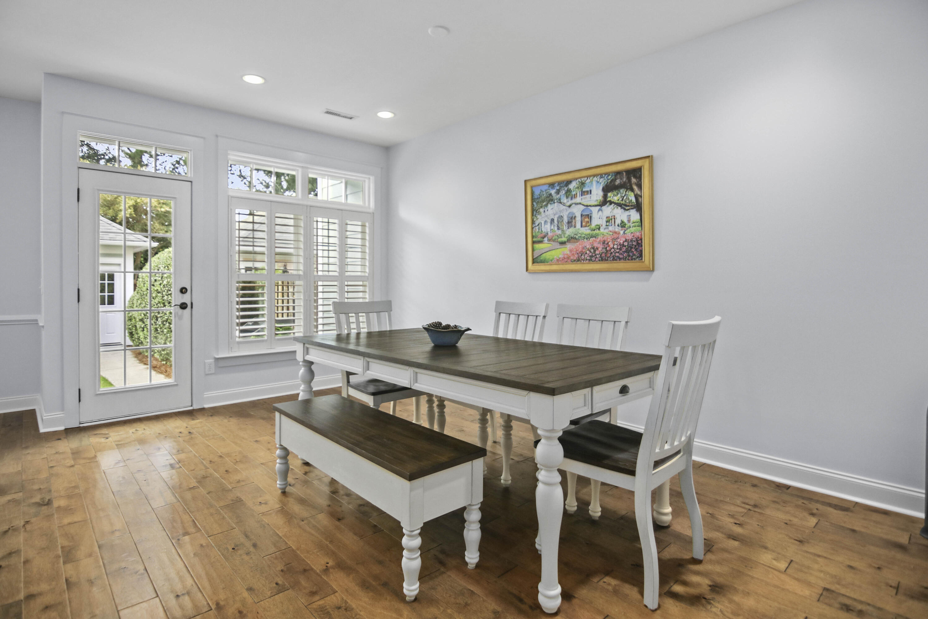 Dining room with a farmhouse table and bench beside plantation-shuttered windows and a glass-paneled door.