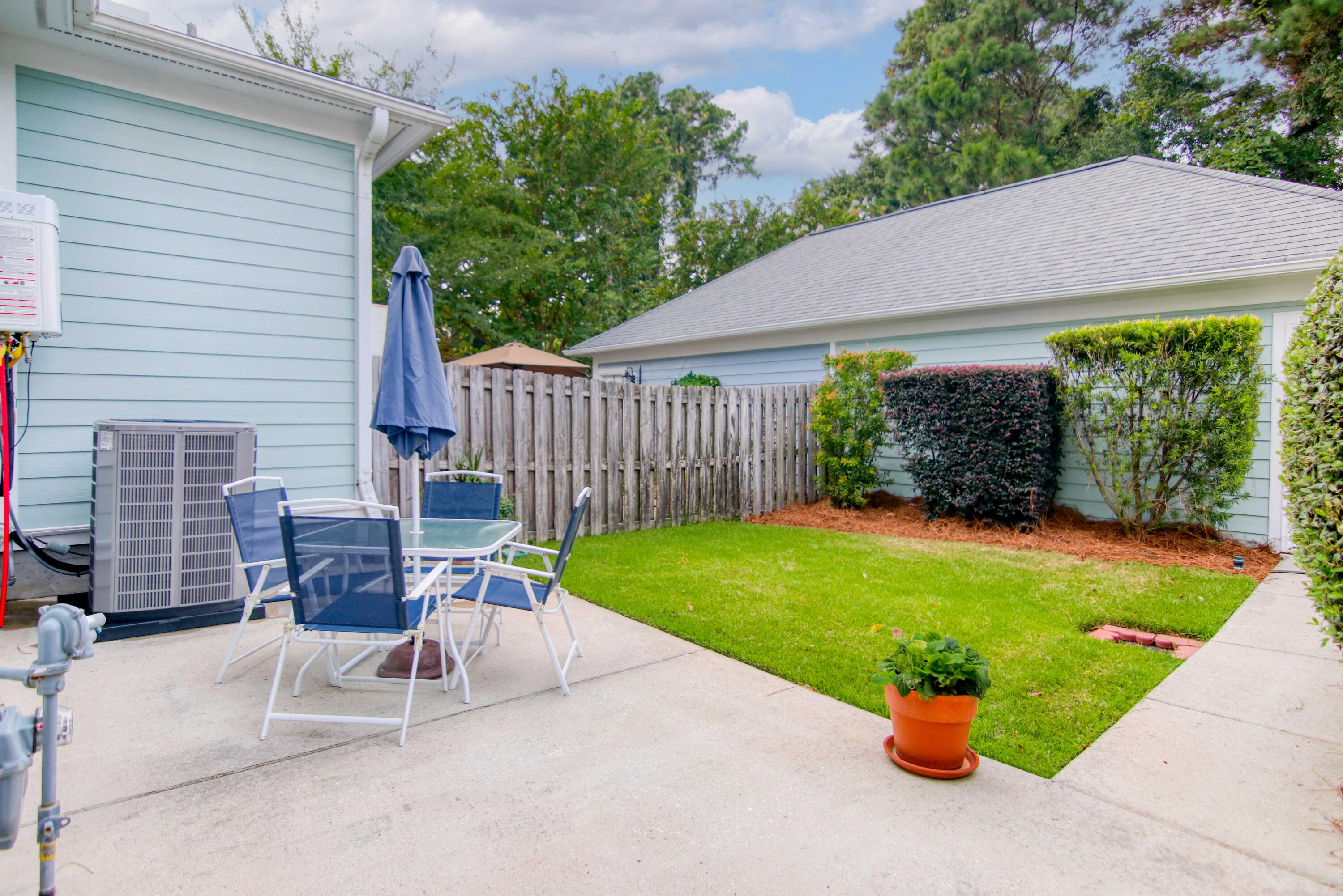 Backyard patio with outdoor table and chairs beside a small lawn and wooden privacy fence.