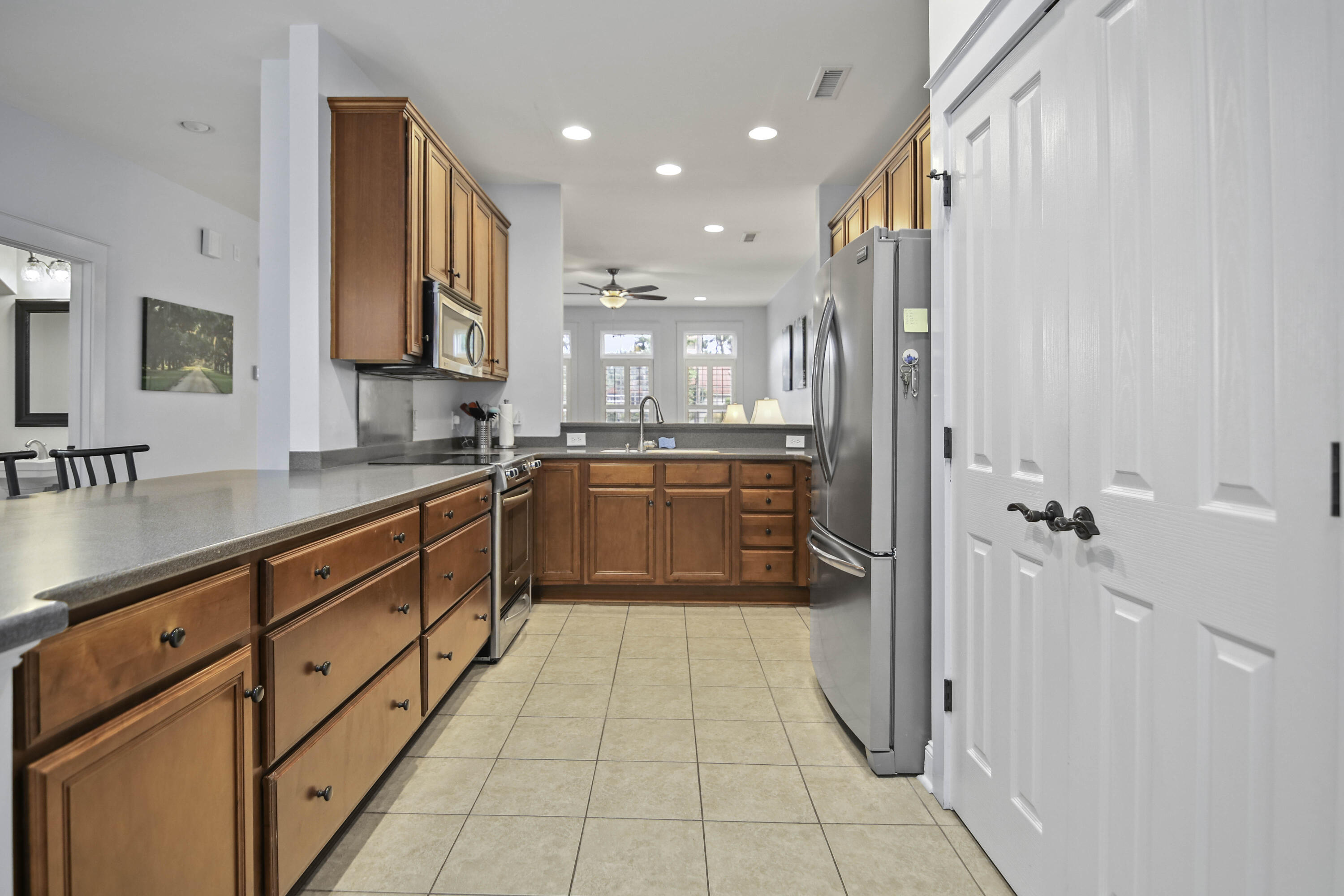 Kitchen with reddish wood cabinets, gray countertops, stainless steel appliances, and white pantry doors.
