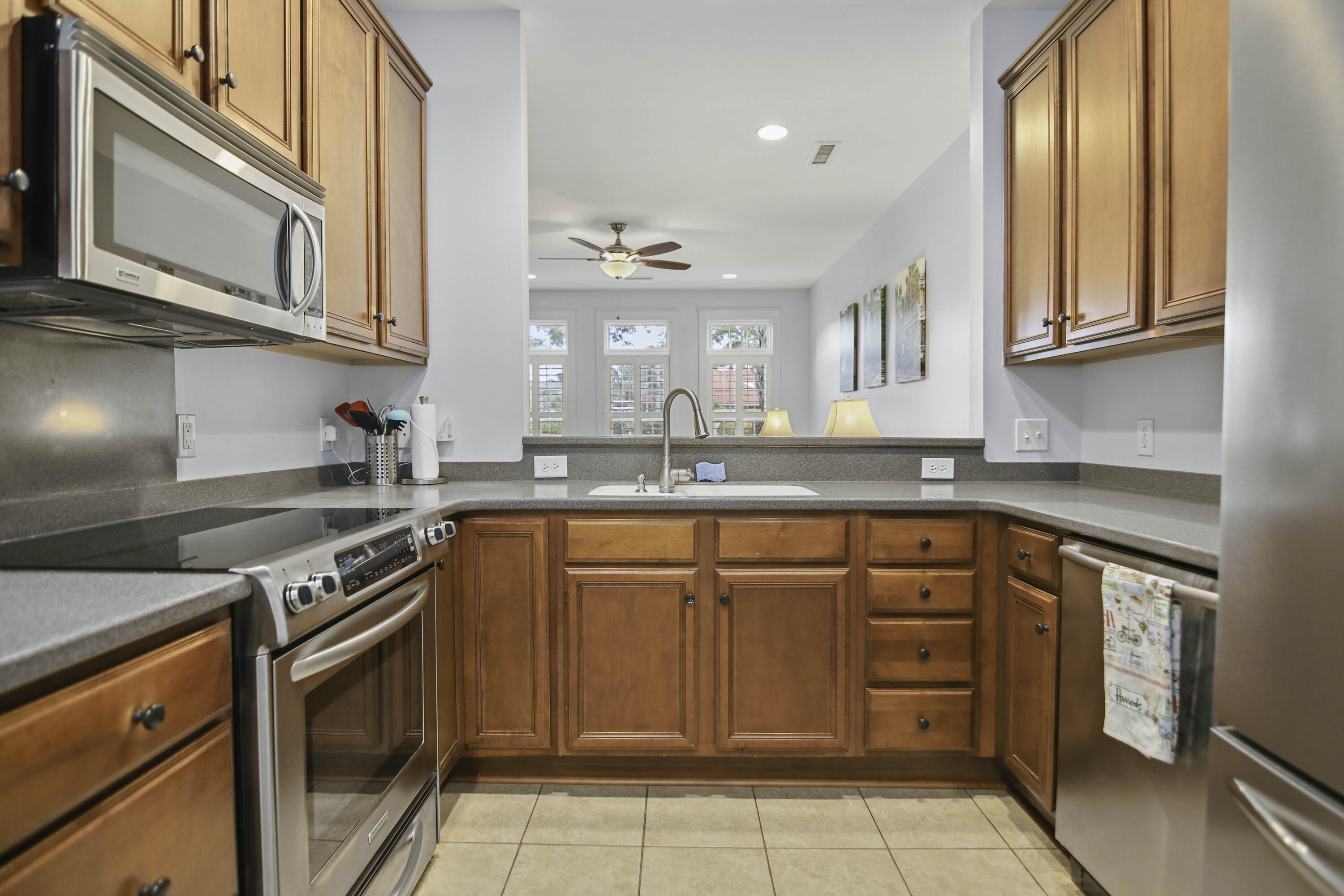Kitchen with warm wood cabinets, gray countertops, stainless steel appliances, and a sink facing the living area.